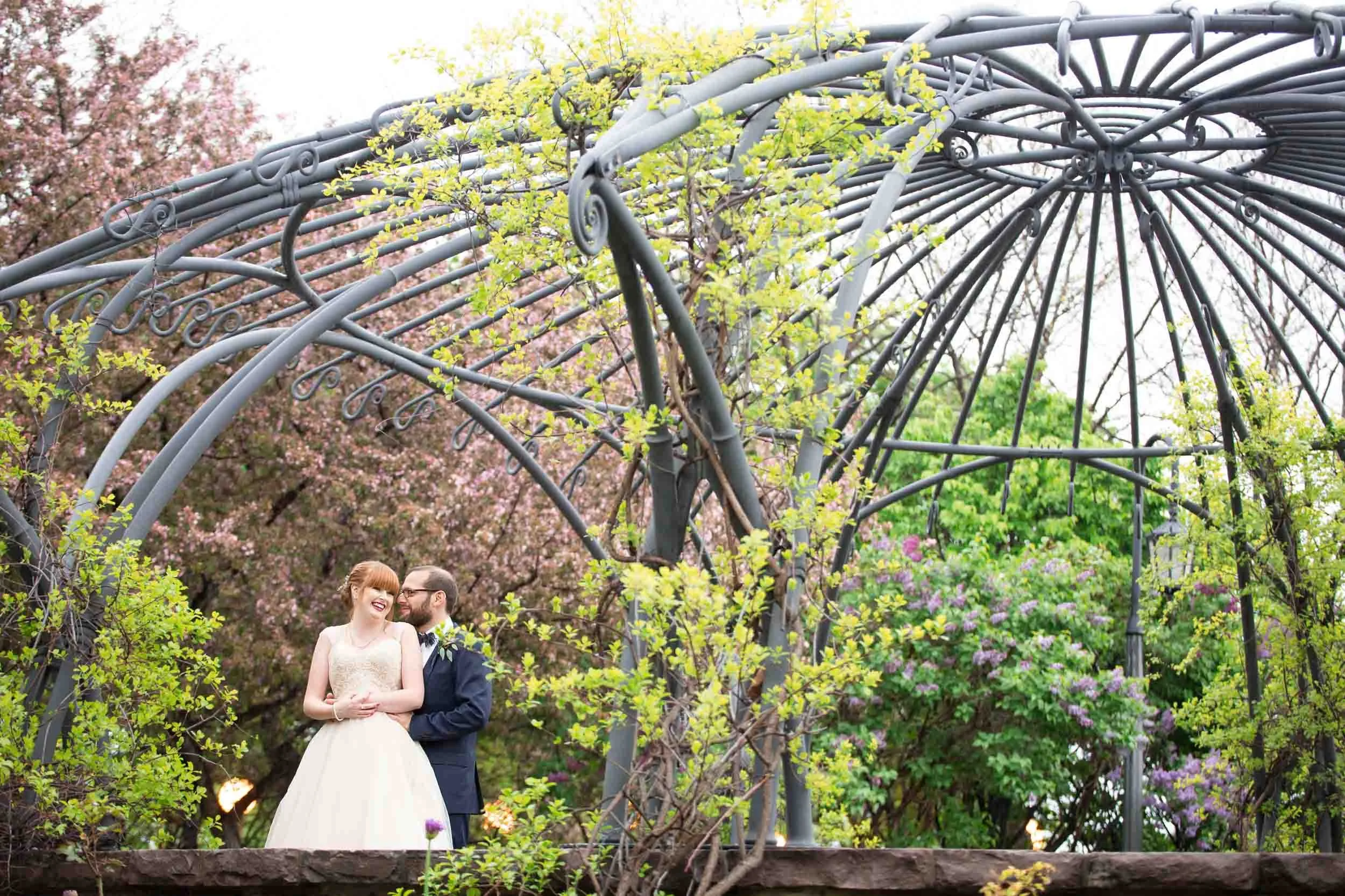 Bride and groom standing together beneath the curved trellis at the Toronto Music Garden (Copy)