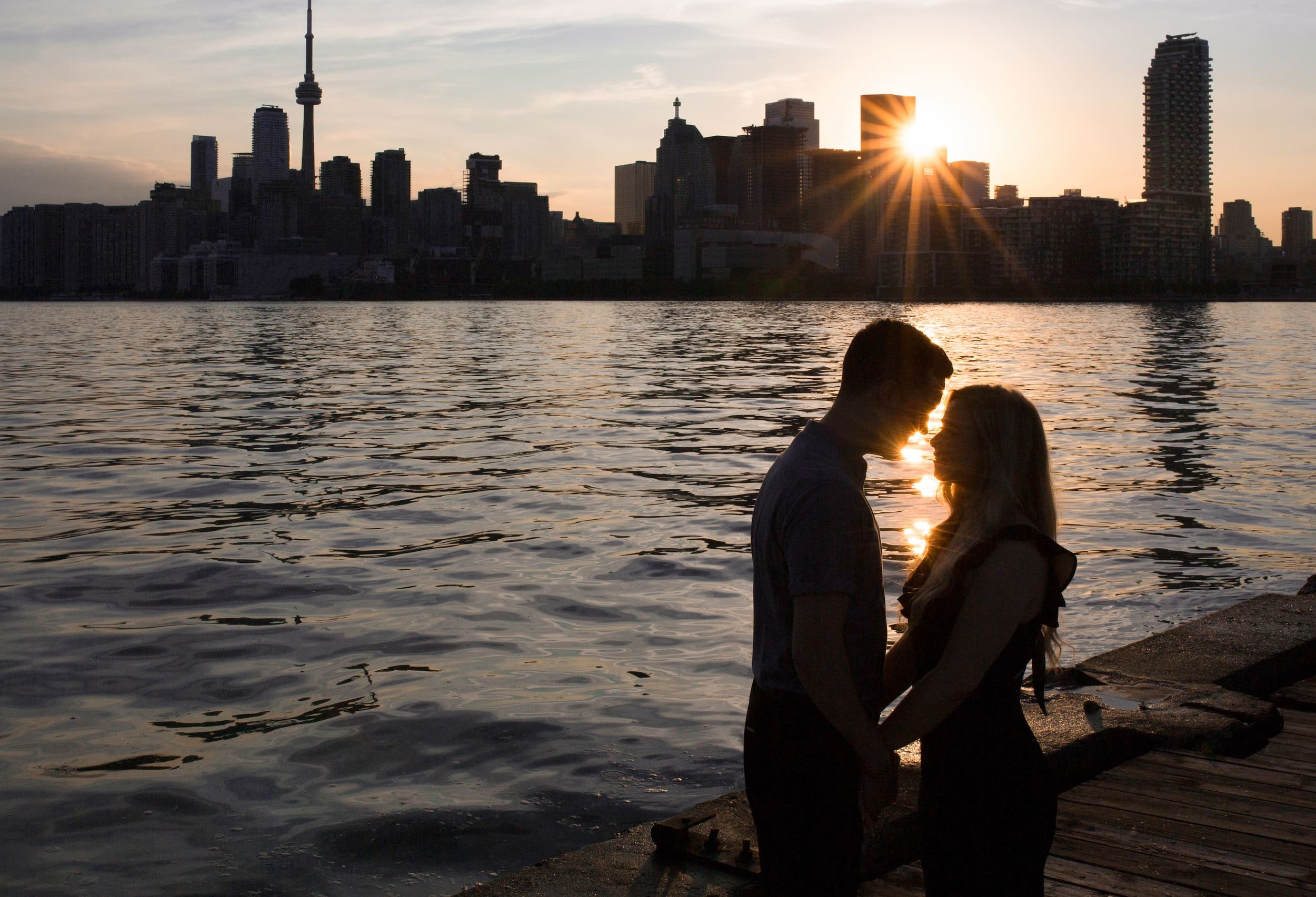 Silhouetted couple standing by the water with the Toronto skyline at sunset during a waterfront engagement (Copy)