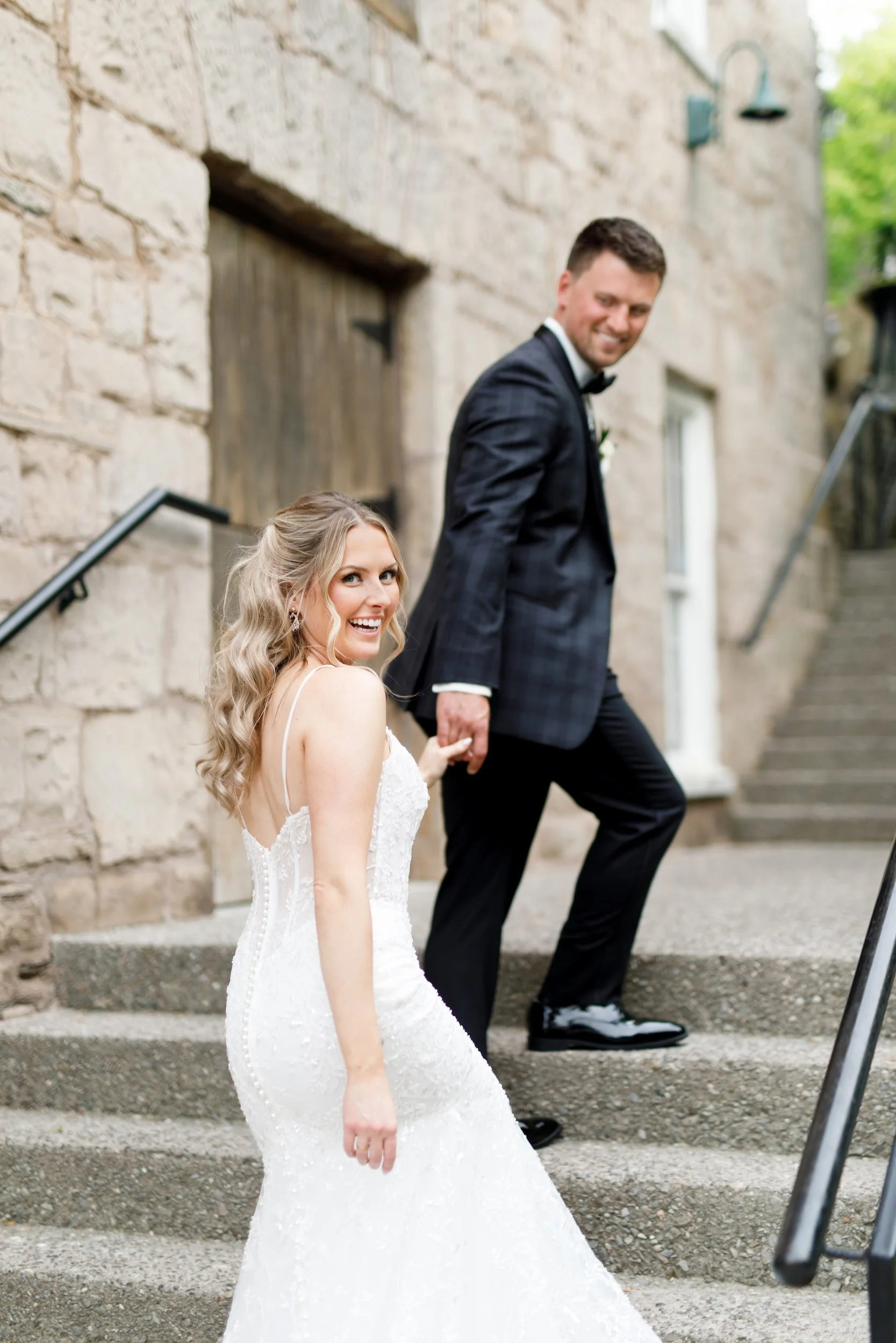 Candid of bride and groom laughing while walking up stone steps at Ancaster Mill wedding venue - View Wedding Portfolio