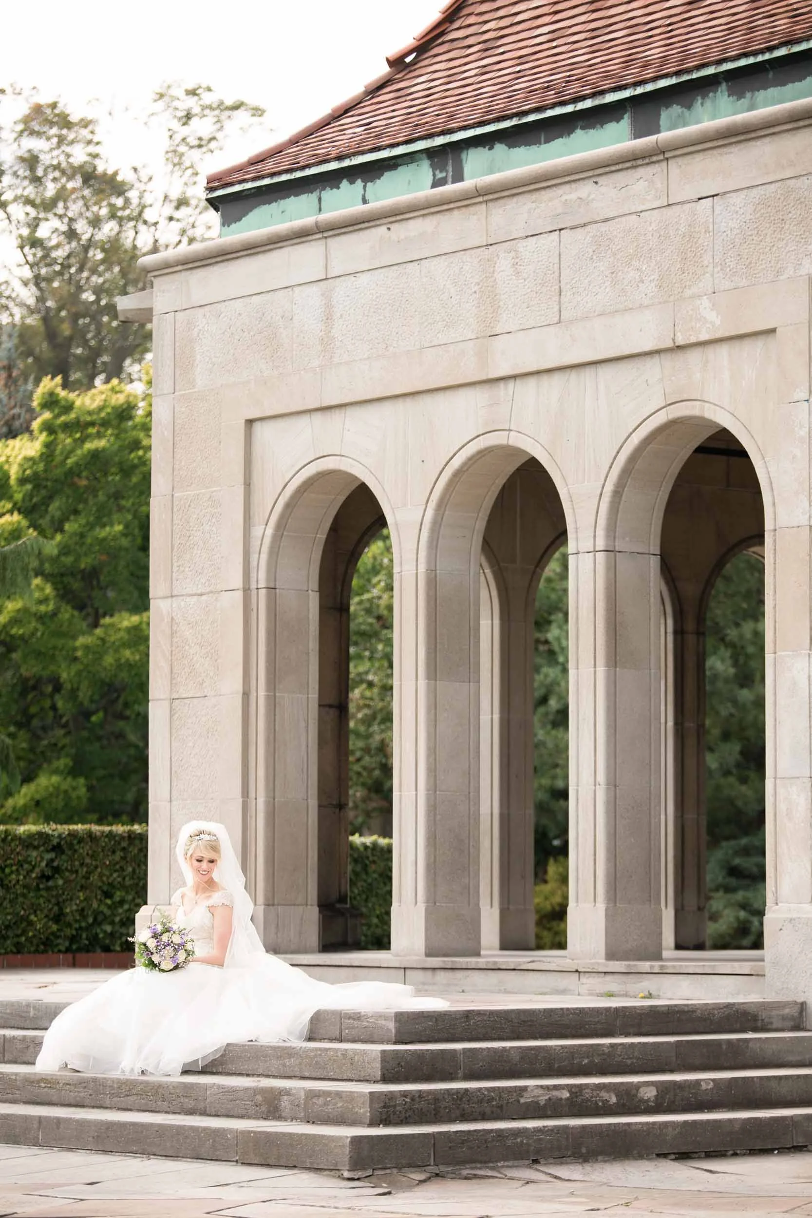 Bride seated on stone steps beneath arches at Oakes Garden Theatre wedding in Niagara Falls (Copy)