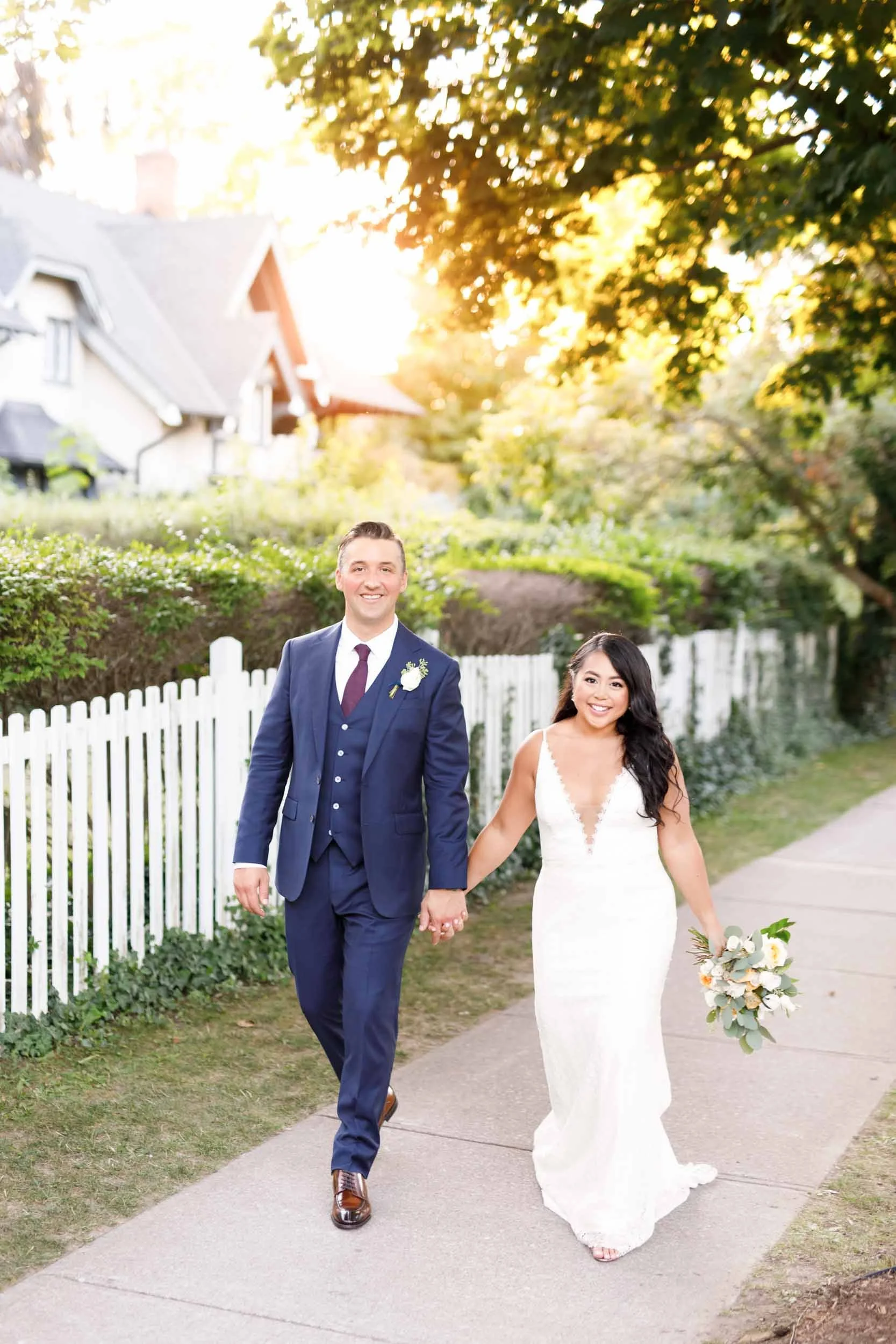 Bride and groom walking hand in hand along white picket fence at sunset in Niagara-on-the-Lake (Copy)