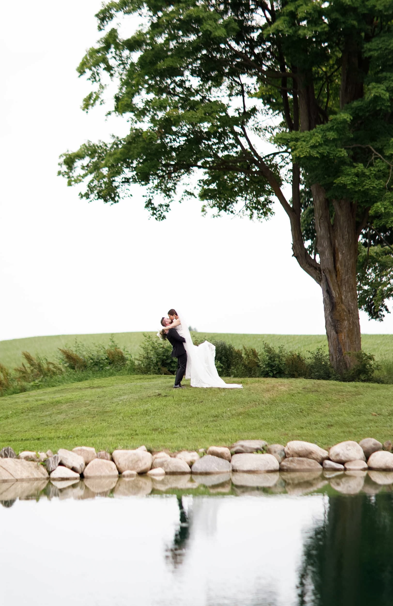 Groom embracing lifting and kissing bride beside pond in the Niagara Region (Copy)