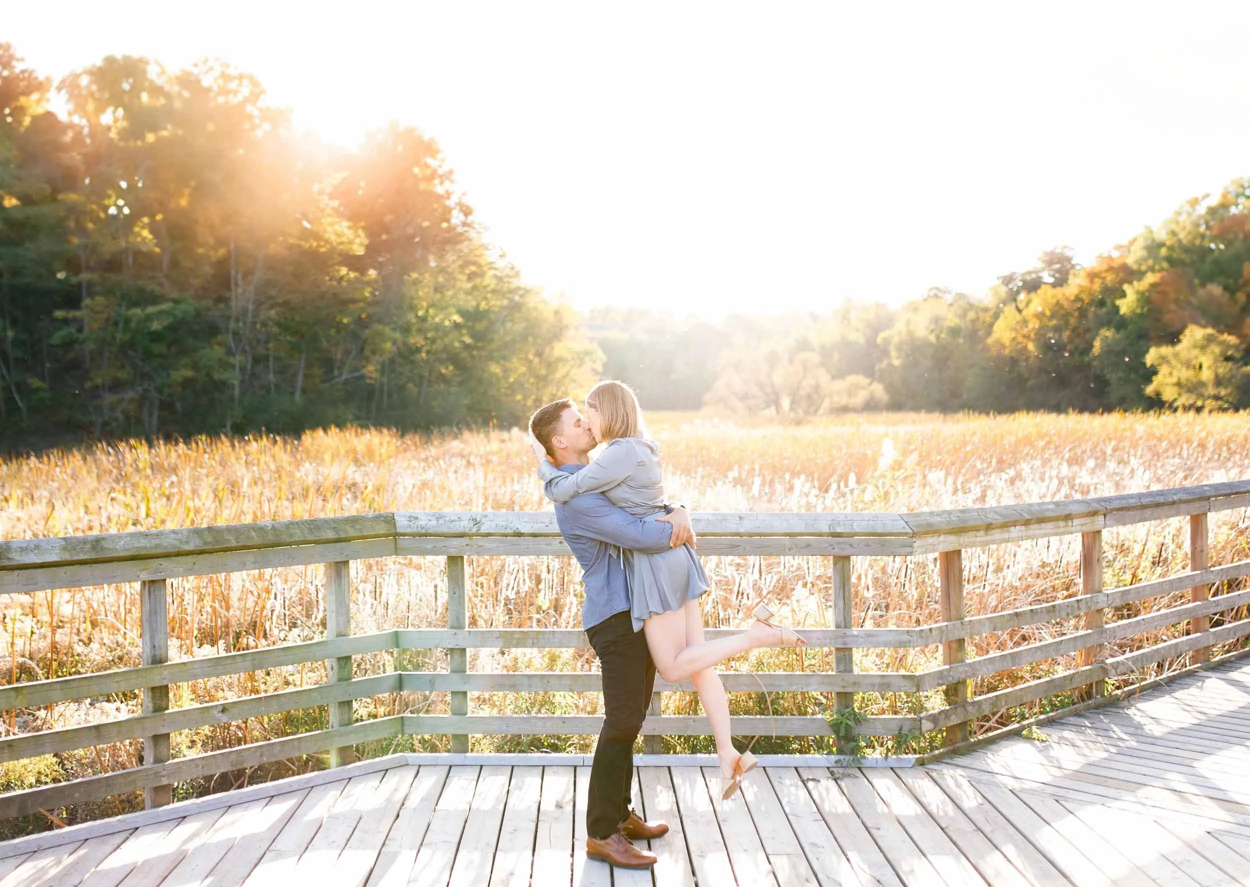 Man lifting his fiancé during golden hour engagement session at Grindstone Marsh Trail in Burlington at sunset (Copy)