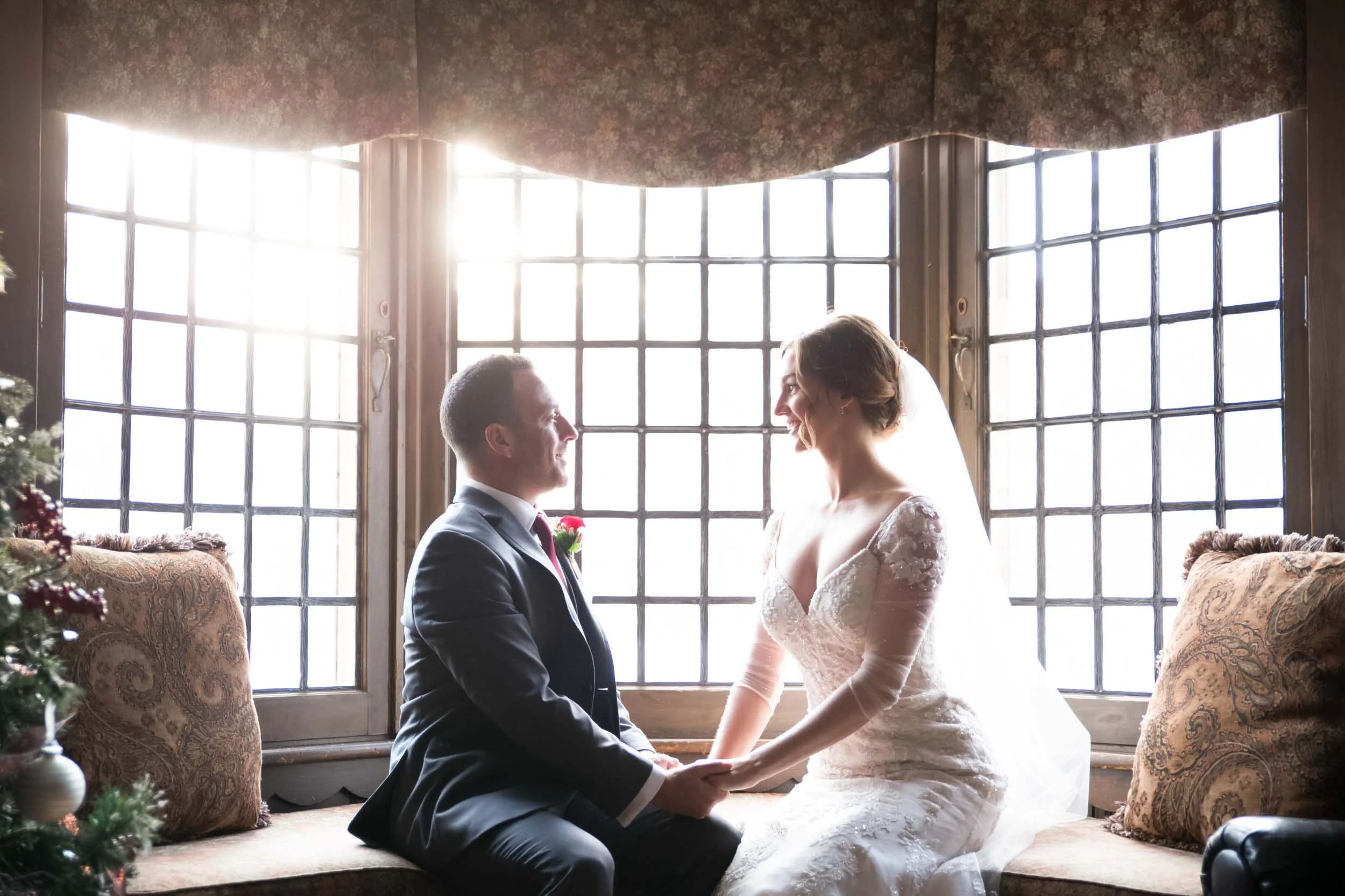 Bride and groom seated by large mullioned windows during winter wedding at Paletta Mansion in Burlington (Copy)