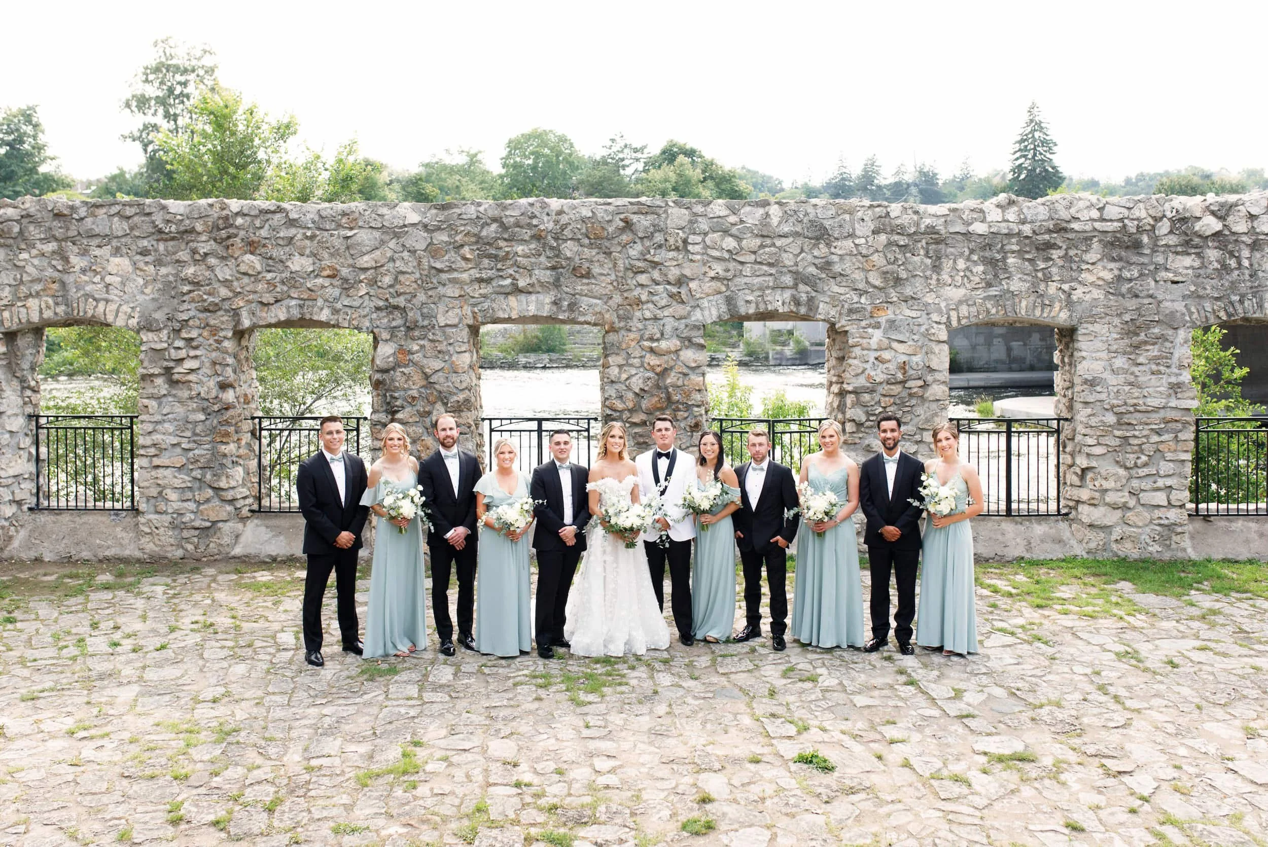 Bride and groom standing with their wedding party at the cobble stone Mill Race Park in Cambridge, Ontario (Copy)