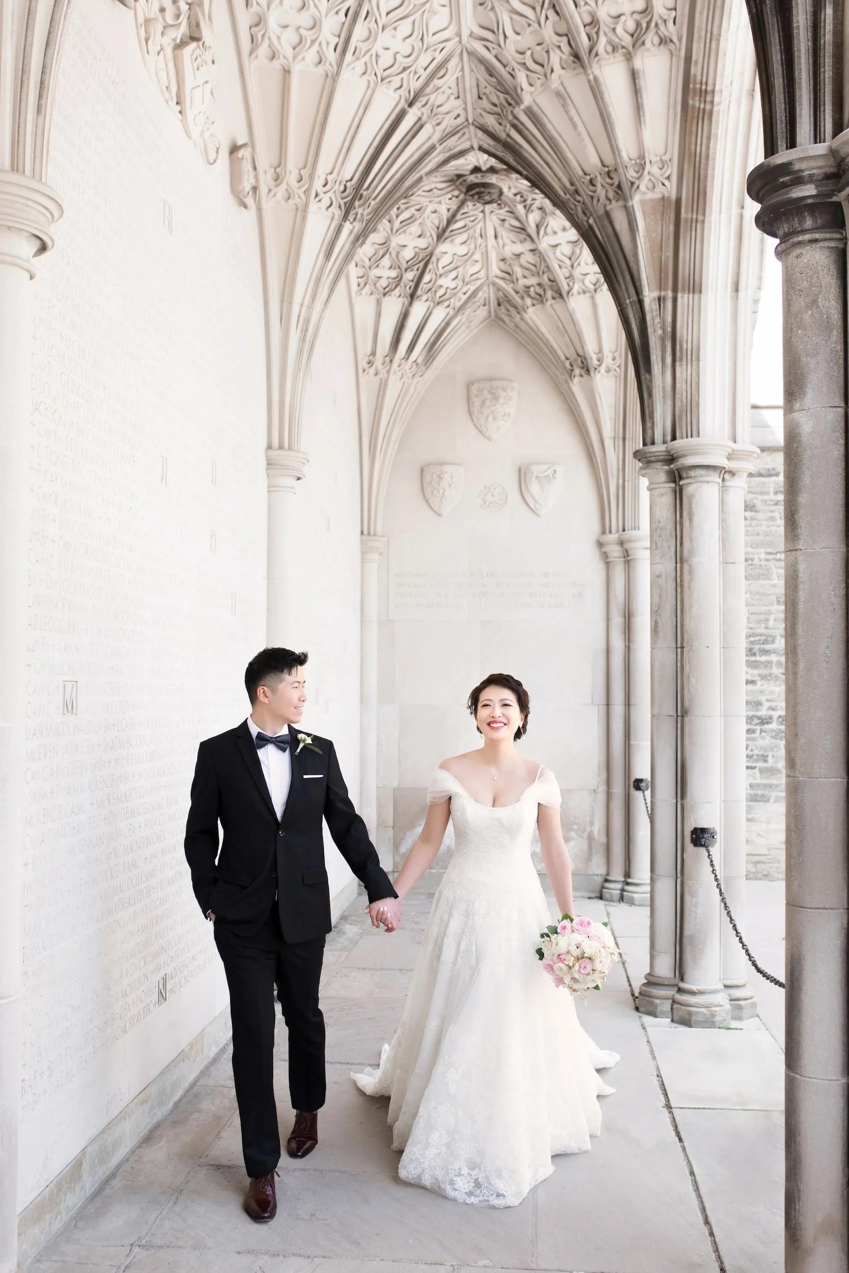 Bride and groom holding hands while walking through Knox College arches at University of Toronto - View Wedding Portfolio