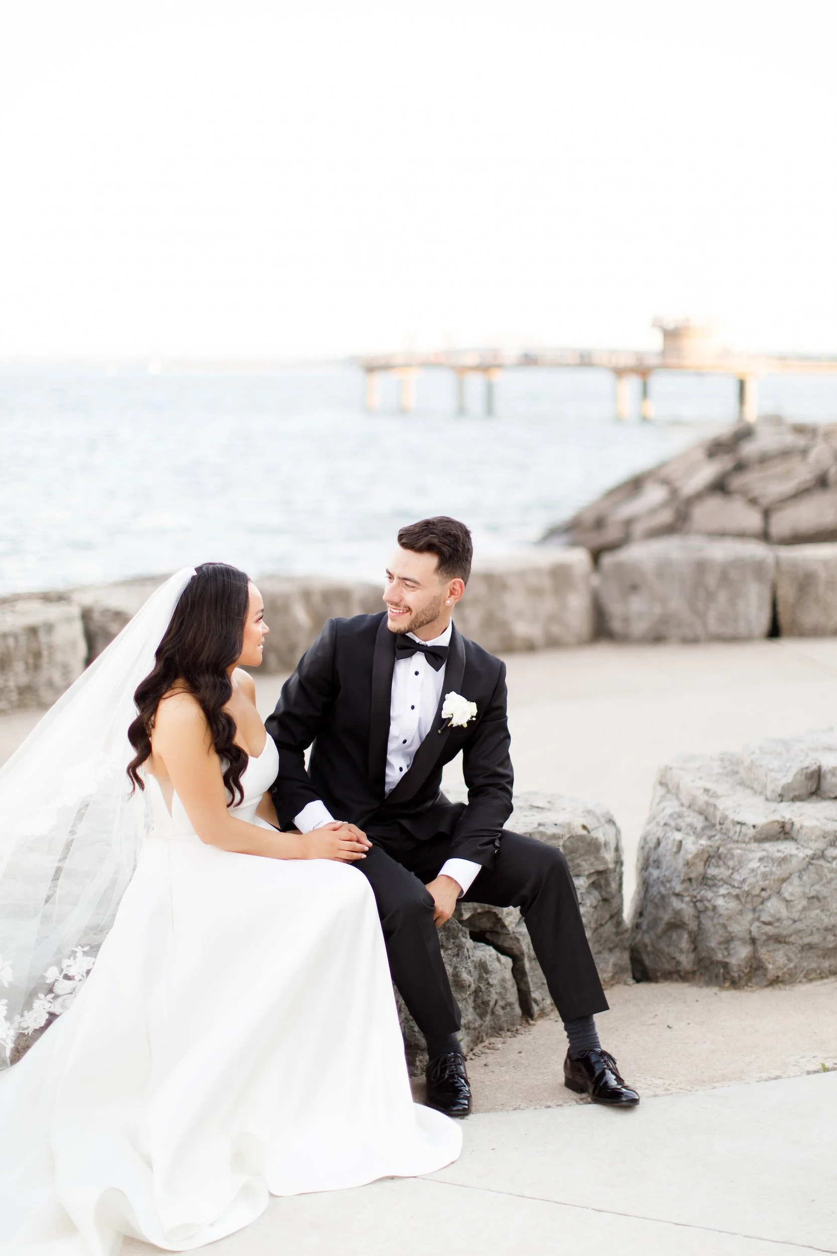 Bride and groom seated on lakeside rocks at Lake Ontario near The Pearle Hotel in Burlington, Ontario