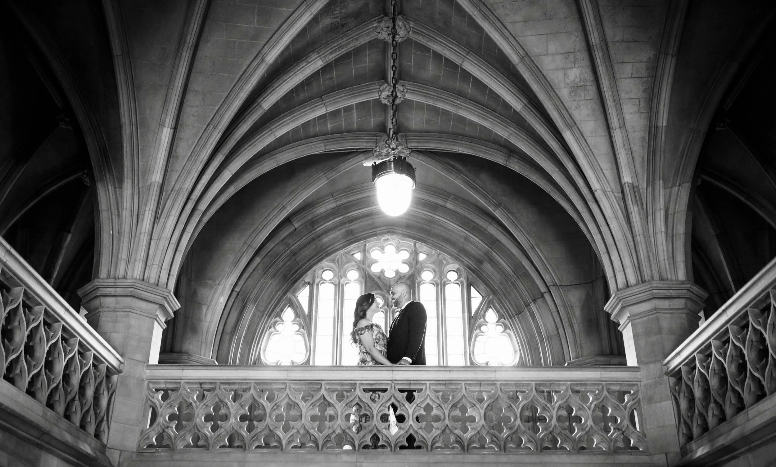 Black and white engagement portrait beneath ribbed Gothic arches at Knox College, University of Toronto in Toronto, Ontario