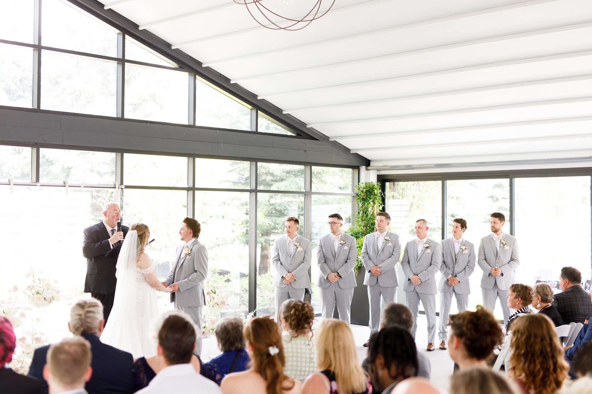 Wedding ceremony with bride, groom, and groomsmen framed by floor-to-ceiling windows at Whistle Bear Golf Club in Cambridge, Ontario