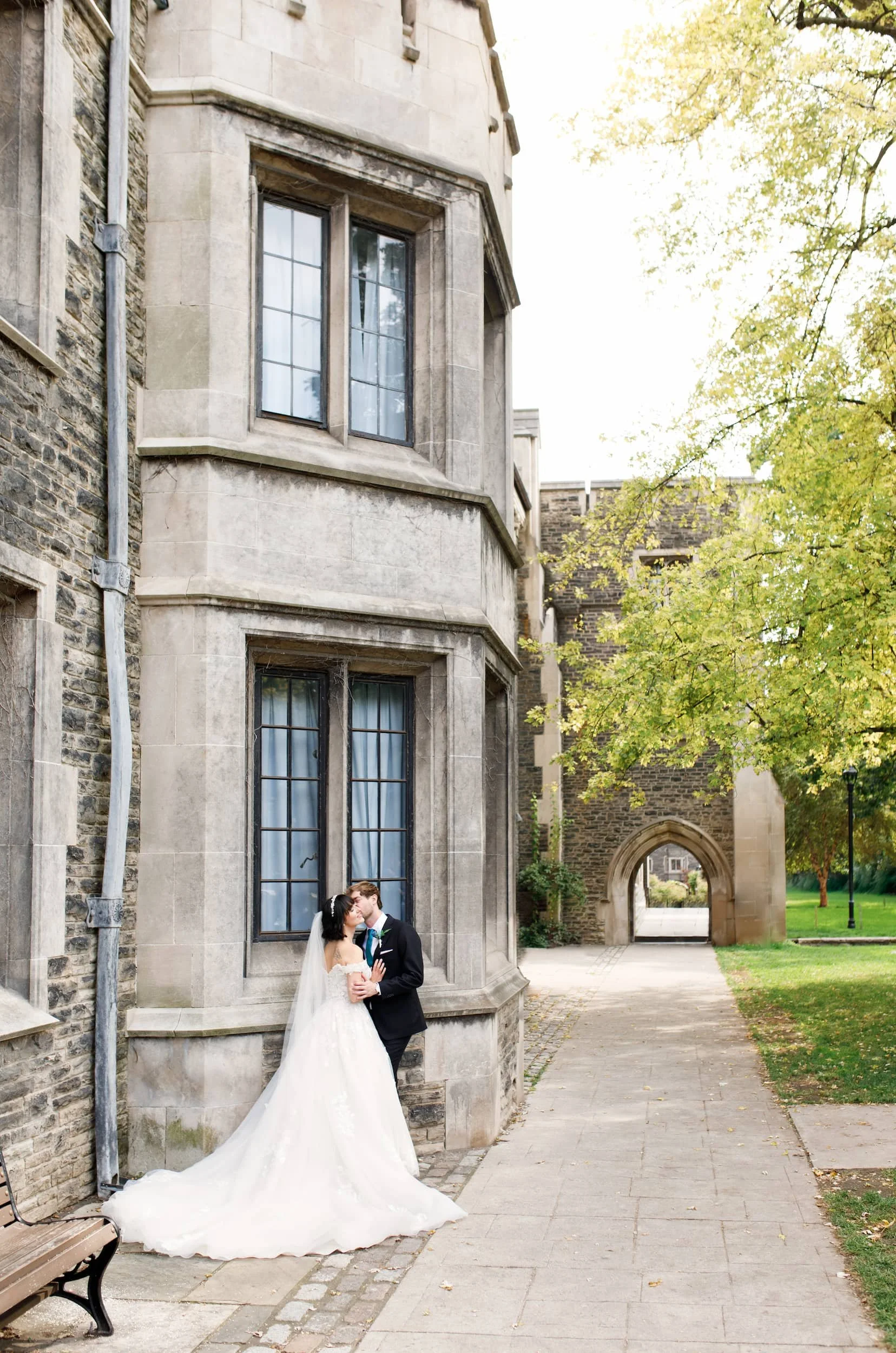 Bride and groom embracing between historic stone buildings at Victoria College, University of Toronto in Toronto, Ontario
