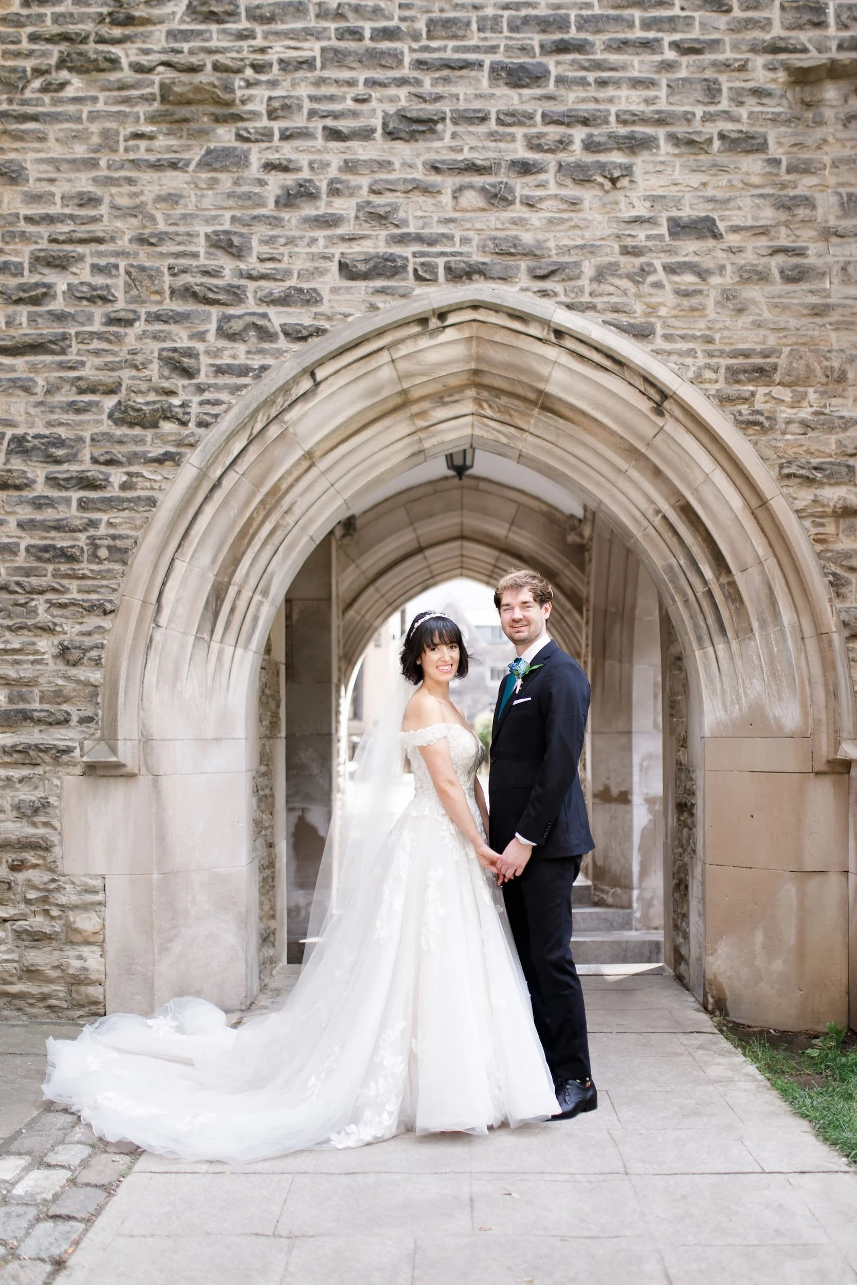 Wedding portrait framed by arched stone doorway at Victoria College, University of Toronto in Toronto, Ontario