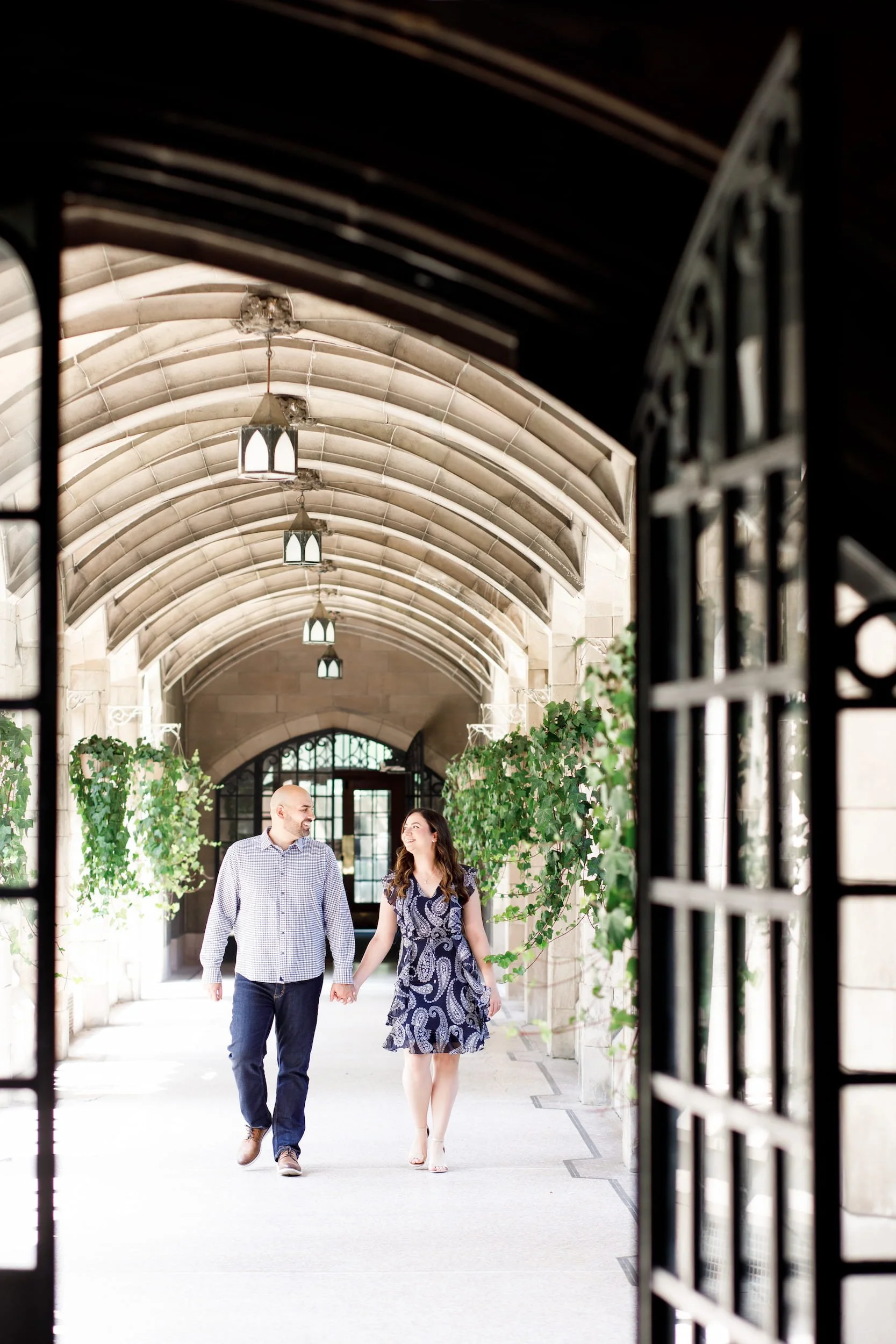 Couple walking through cloister corridor during engagement session at Knox College, University of Toronto in Toronto, Ontario