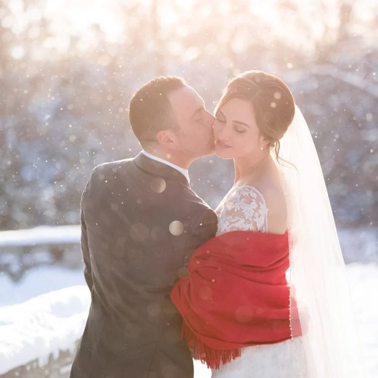 Groom kissing the bride’s cheek during a snow-covered winter wedding at Paletta Mansion in Burlington, Ontario