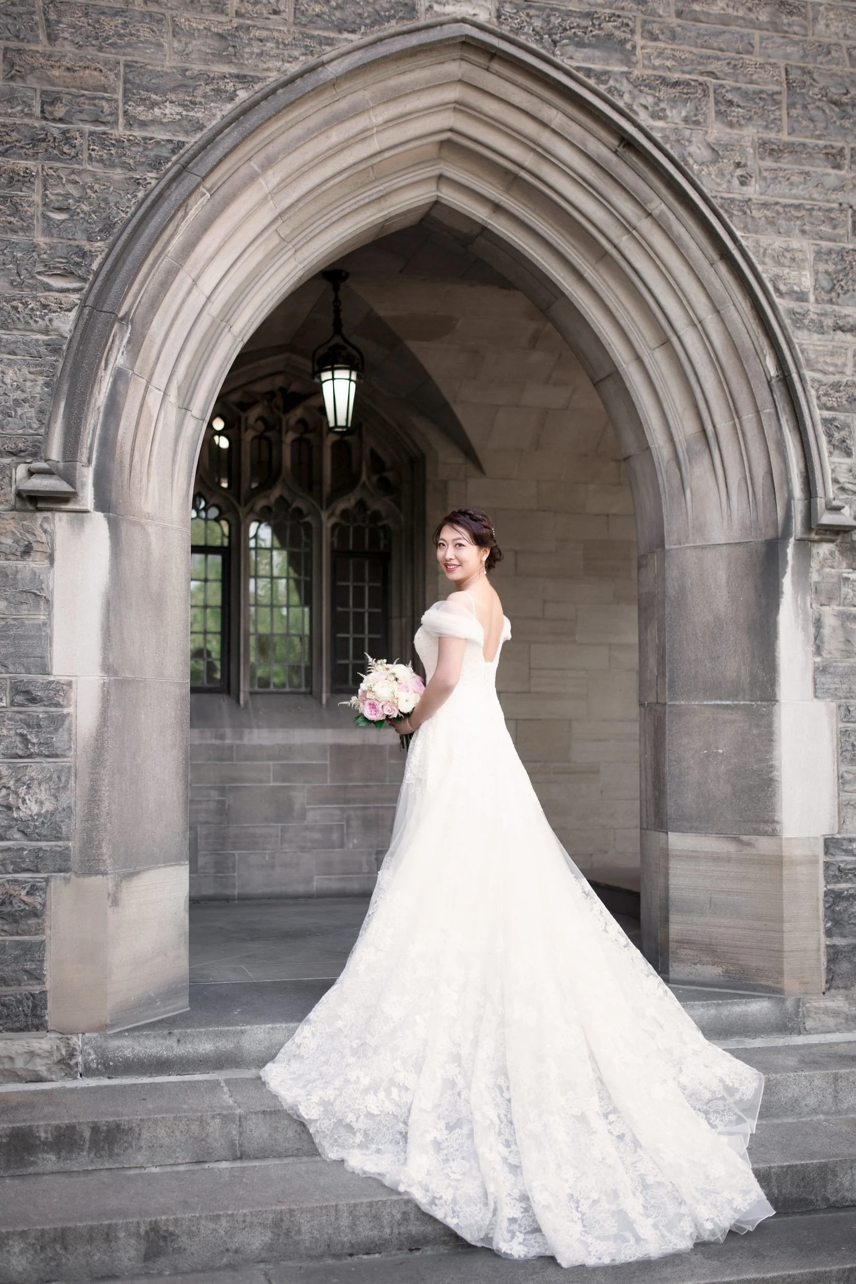 Bride standing beneath historic stone arch at Knox College, University of Toronto in Toronto, Ontario