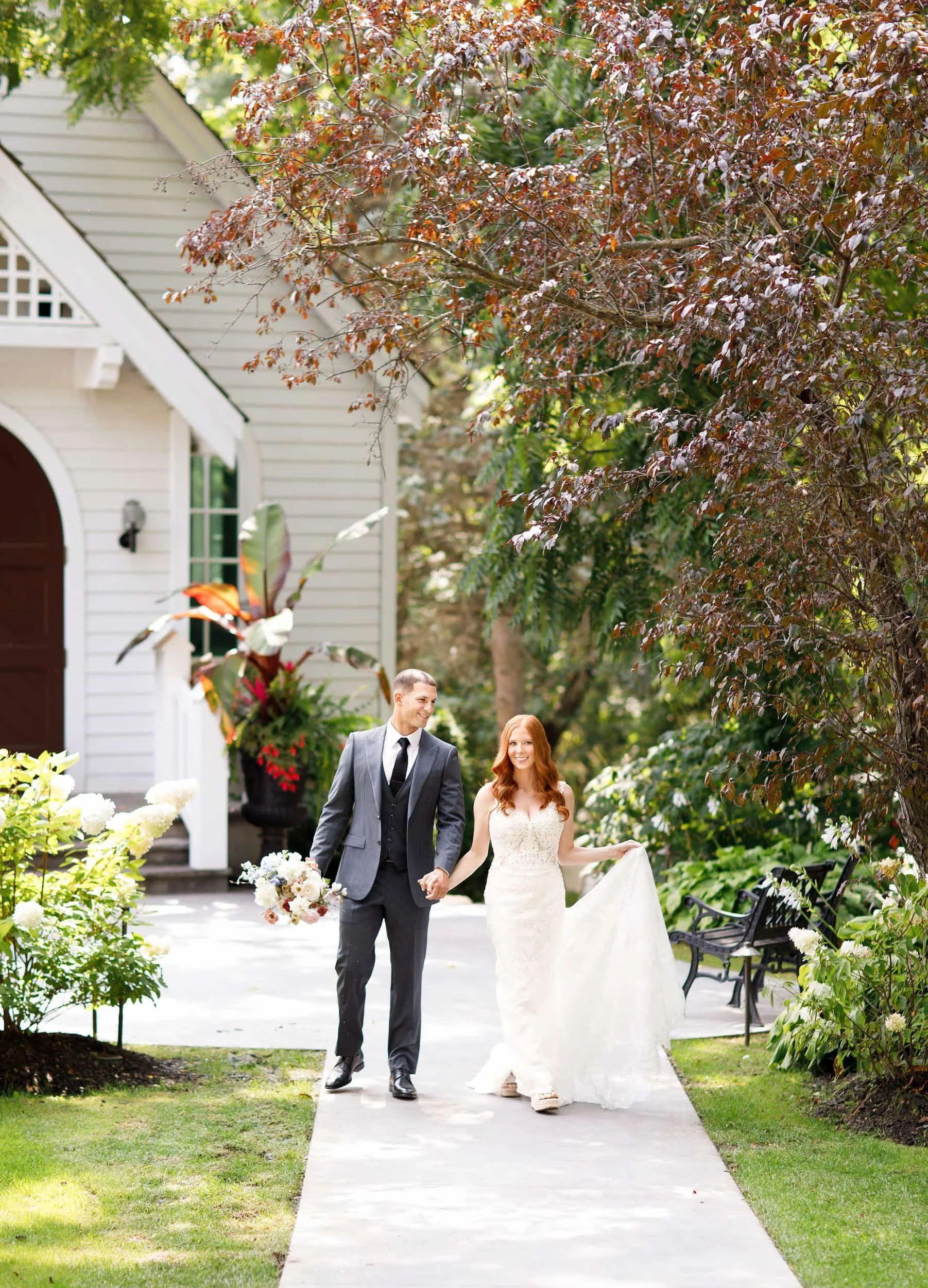 Bride and groom holding hands and walking in front of white chapel at The Doctor’s House in Kleinburg, Ontario