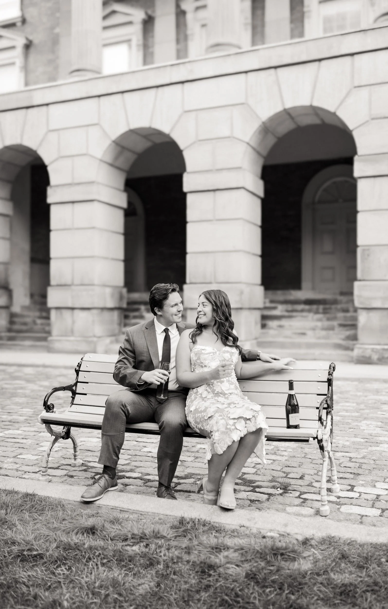 Black and white engagement portrait beneath stone arches at Osgoode Hall courthouse