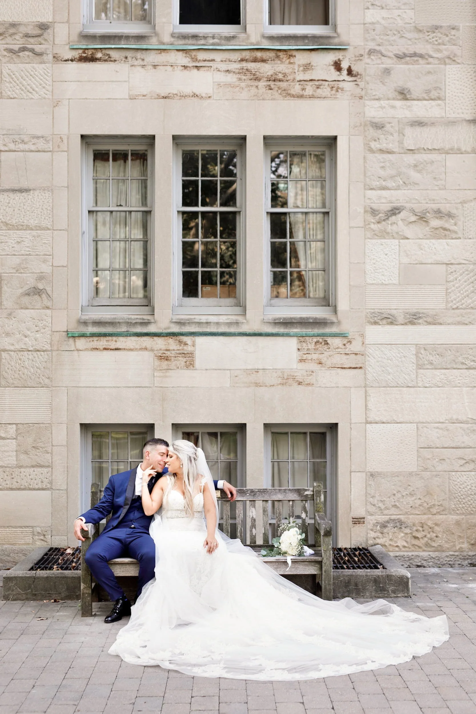 Bride and groom seated on stone bench at St. Michael’s College, University of Toronto in Toronto, Ontario