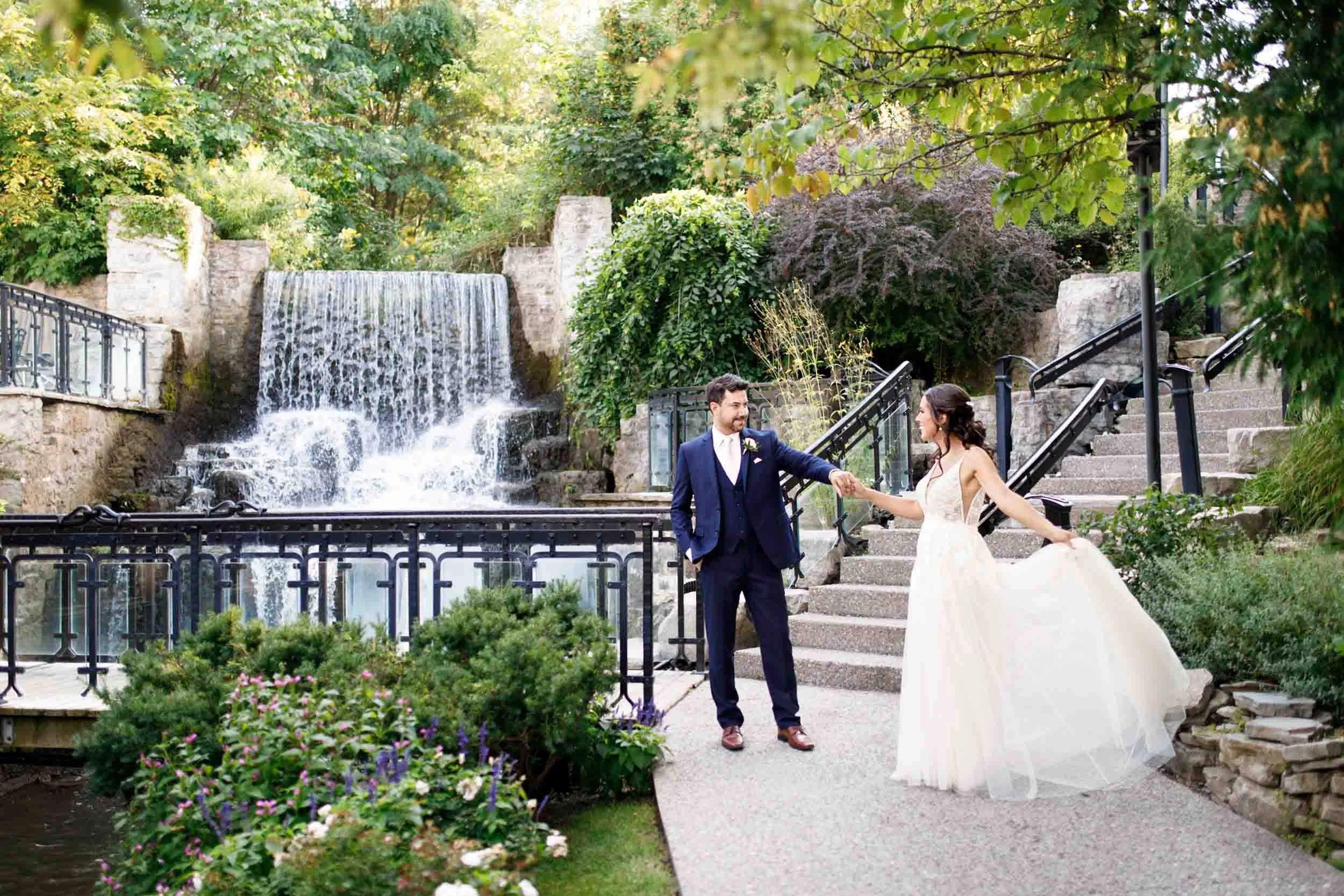 Bride and groom walking near the waterfall at the Ancaster Mill in Ancaster, Ontario