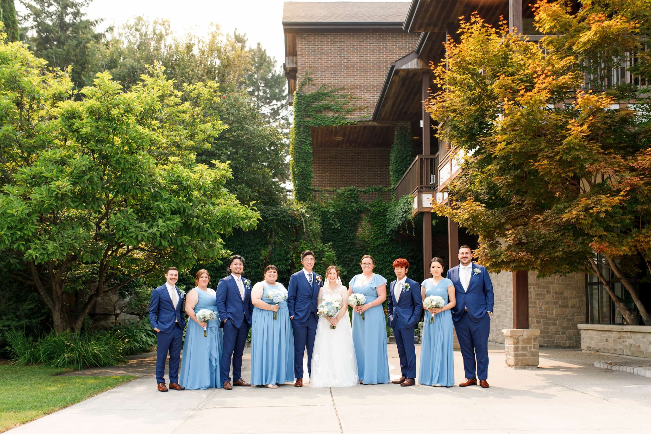 Wedding party in blue attire gathered outside ivy-covered Manor facade in King, Ontario