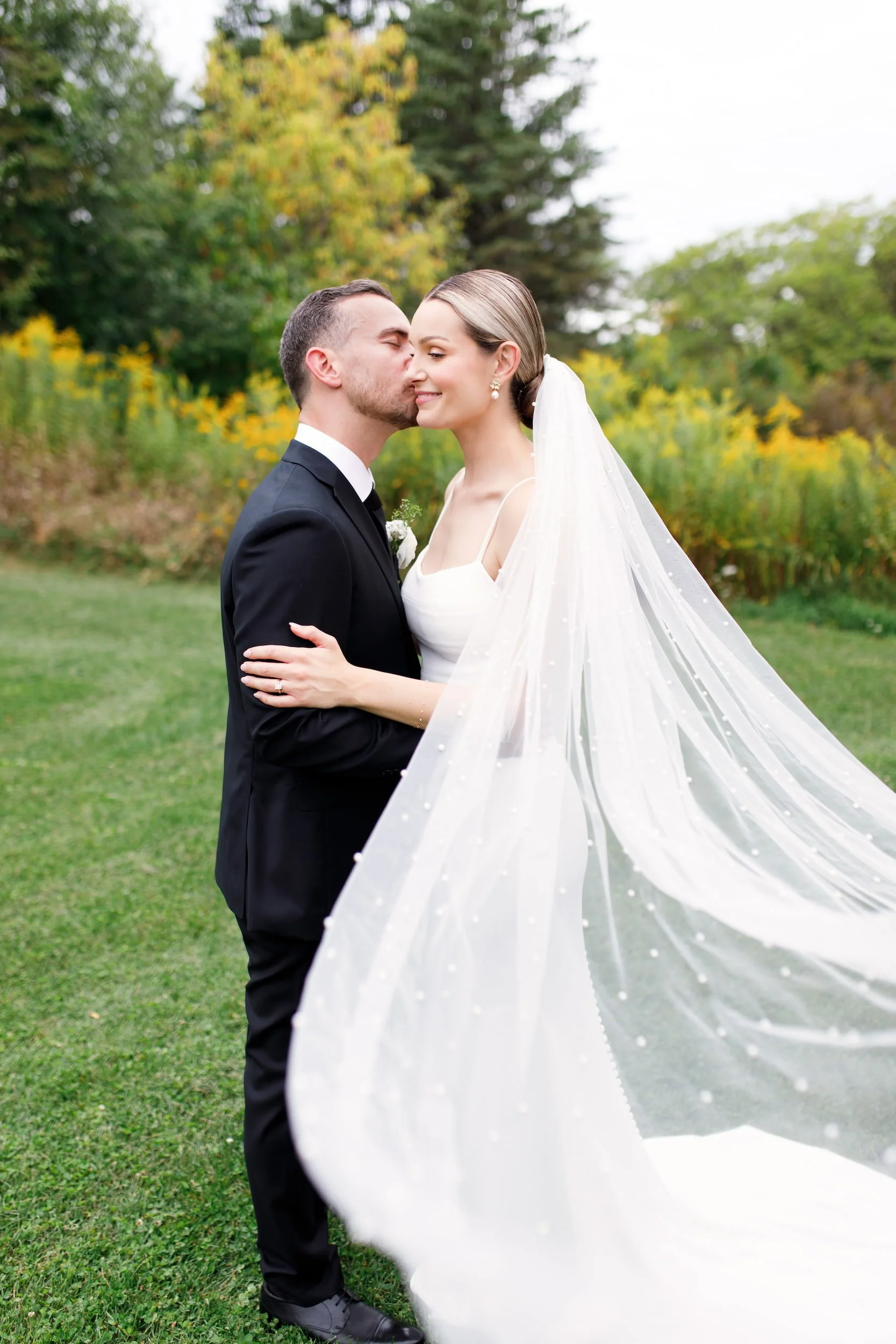 Bride and groom embracing with flowing veil during outdoor portraits at The Manor Event Venue wedding in King, Ontario
