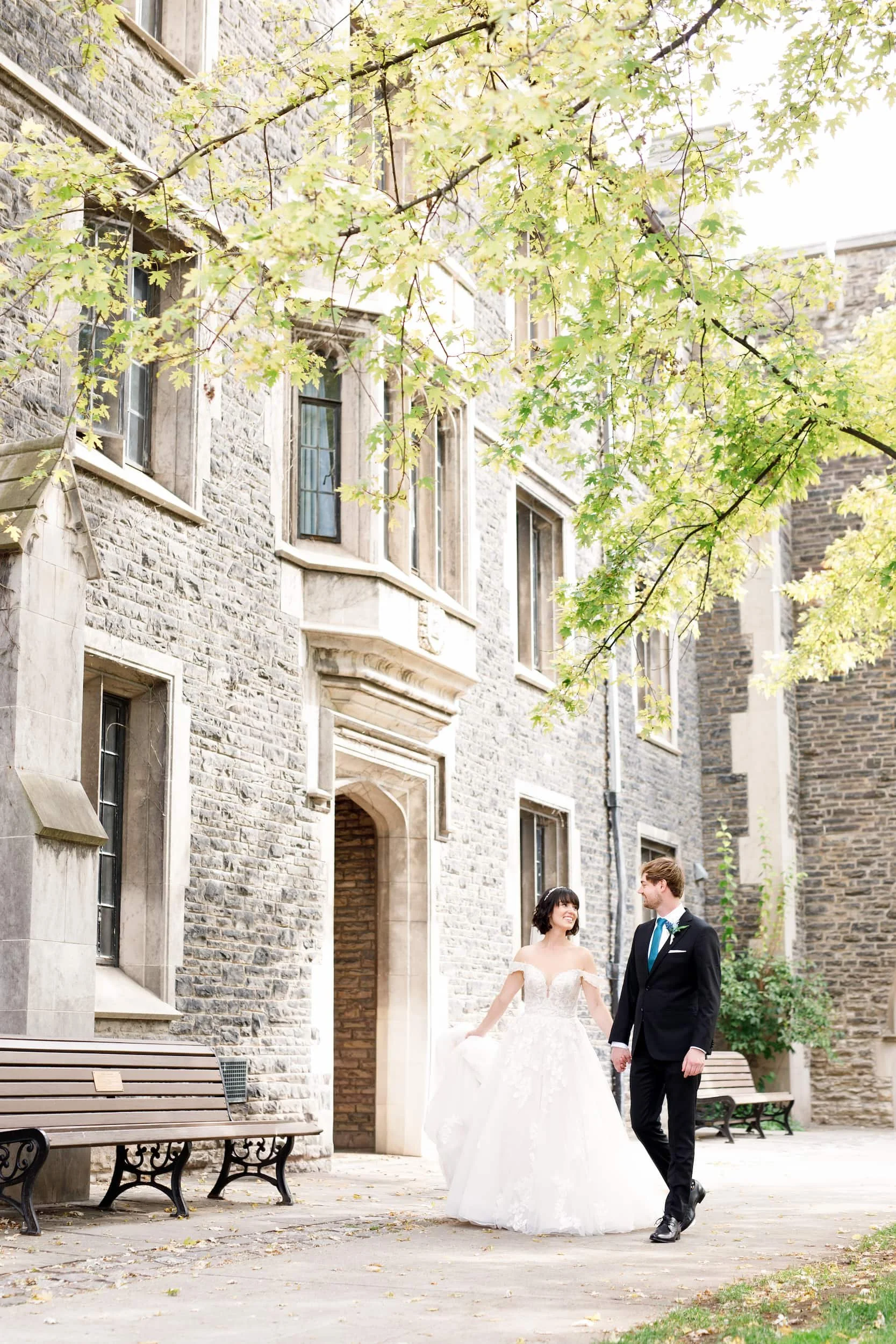 Bride and groom walking hand-in-hand along St. Michael's College at the University of Toronto 