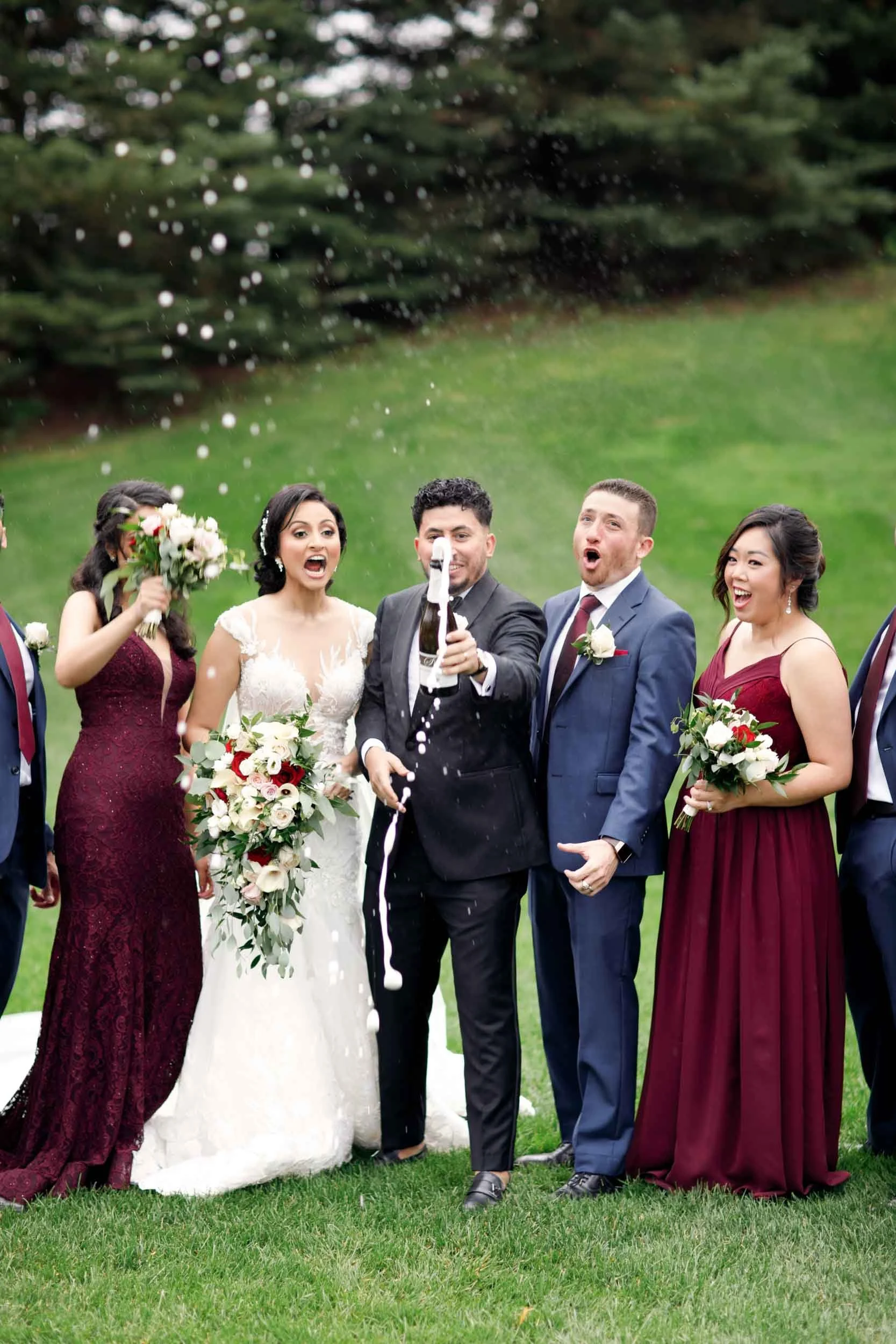 Wedding party celebrating with champagne spray on the lawn at The Manor Event Venue in King, Ontario