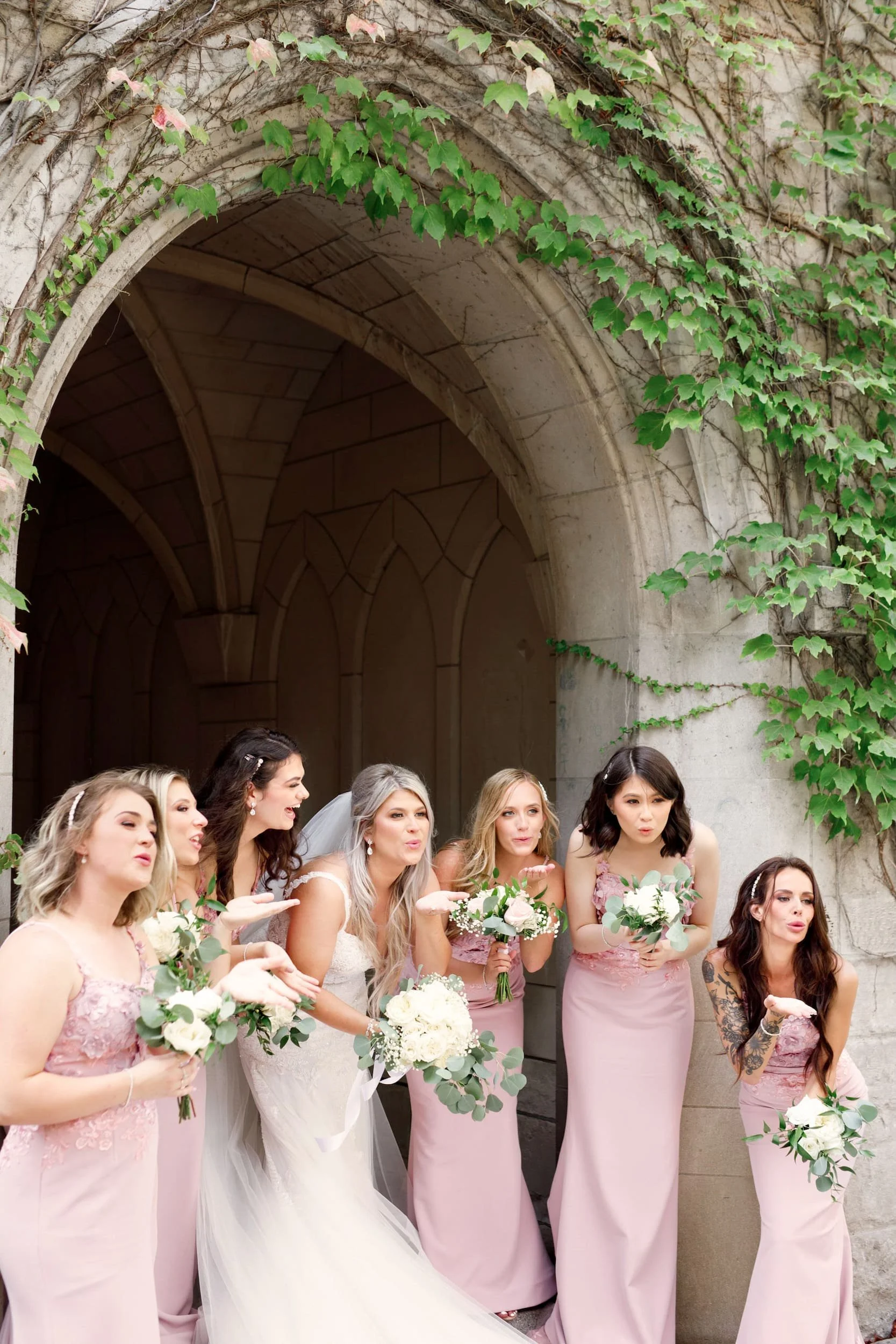 Bridesmaids reacting playfully beneath stone arch at St. Michael’s College, University of Toronto in Toronto, Ontario