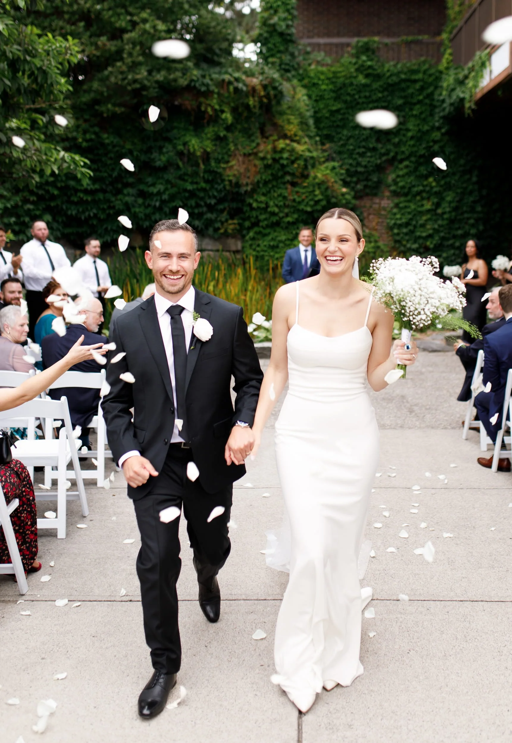 Newlyweds walking down the aisle as guests toss petals at The Manor Event Venue wedding in King, Ontario