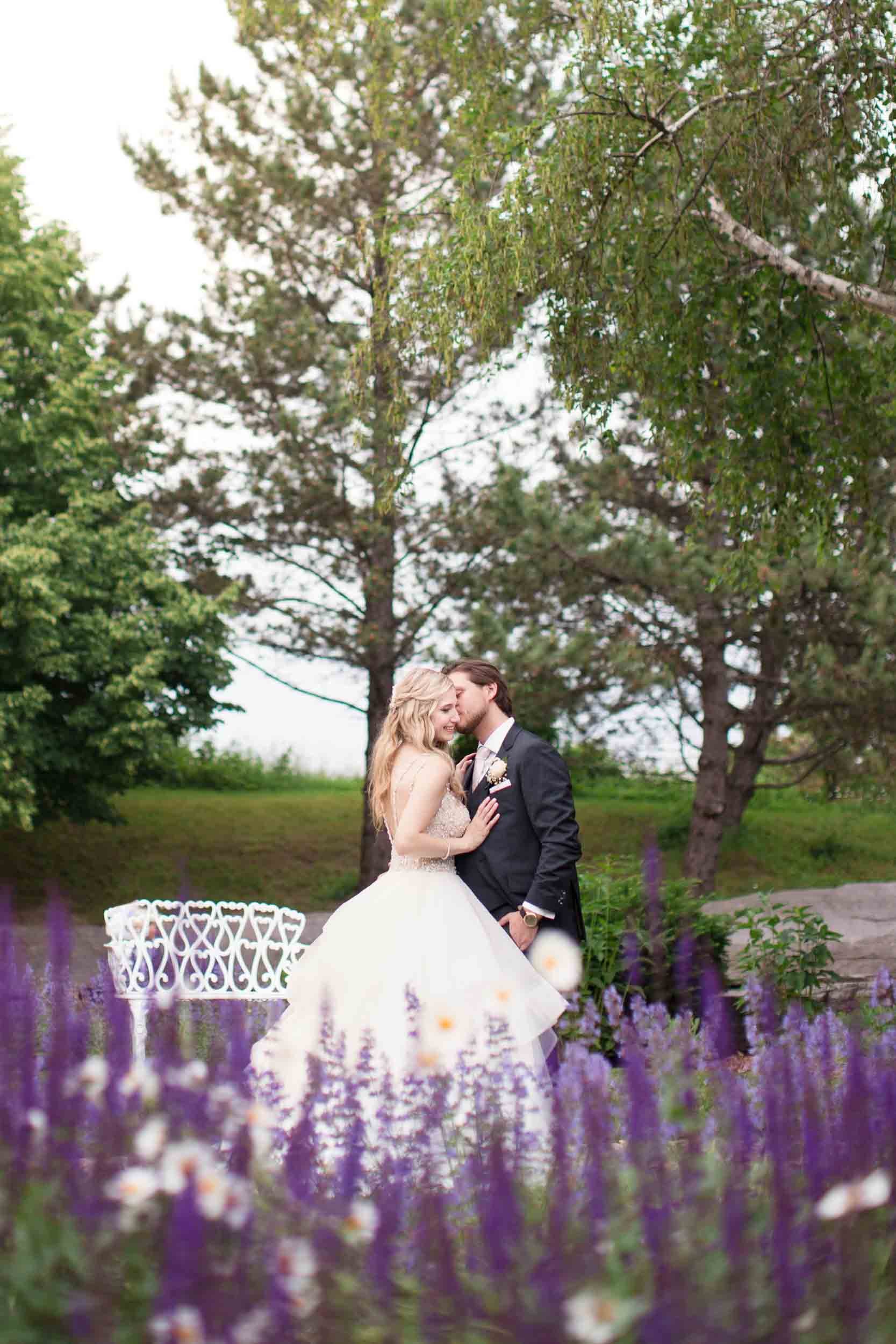 Bride and groom seated on white bench surrounded by florals at The Manor Event Venue wedding in King, Ontario