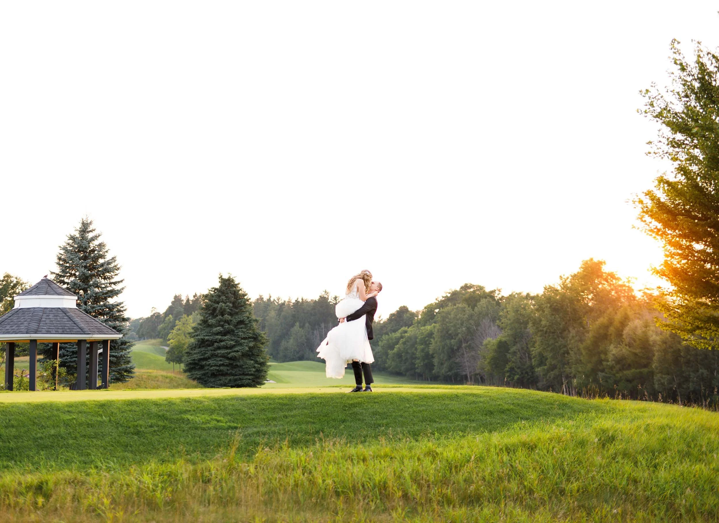 Bride lifted and groom embracing her on the golf course at sunset at Whistle Bear Golf Club in Cambridge, Ontario