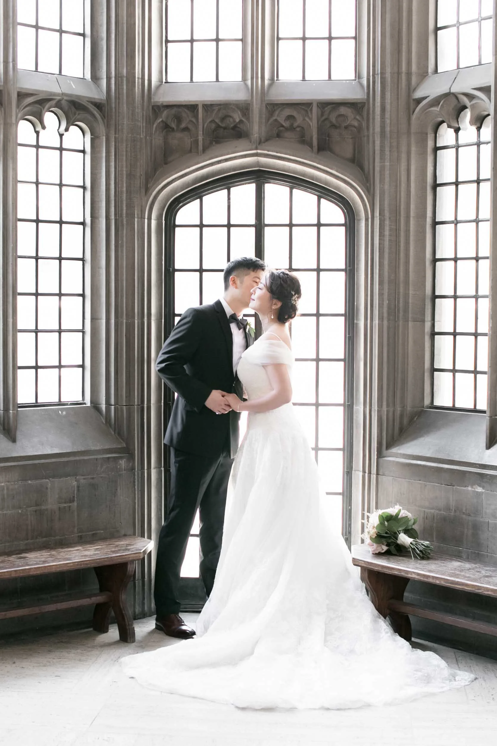 Bride and groom embracing beside arched stone window at Knox College, University of Toronto in Toronto, Ontario
