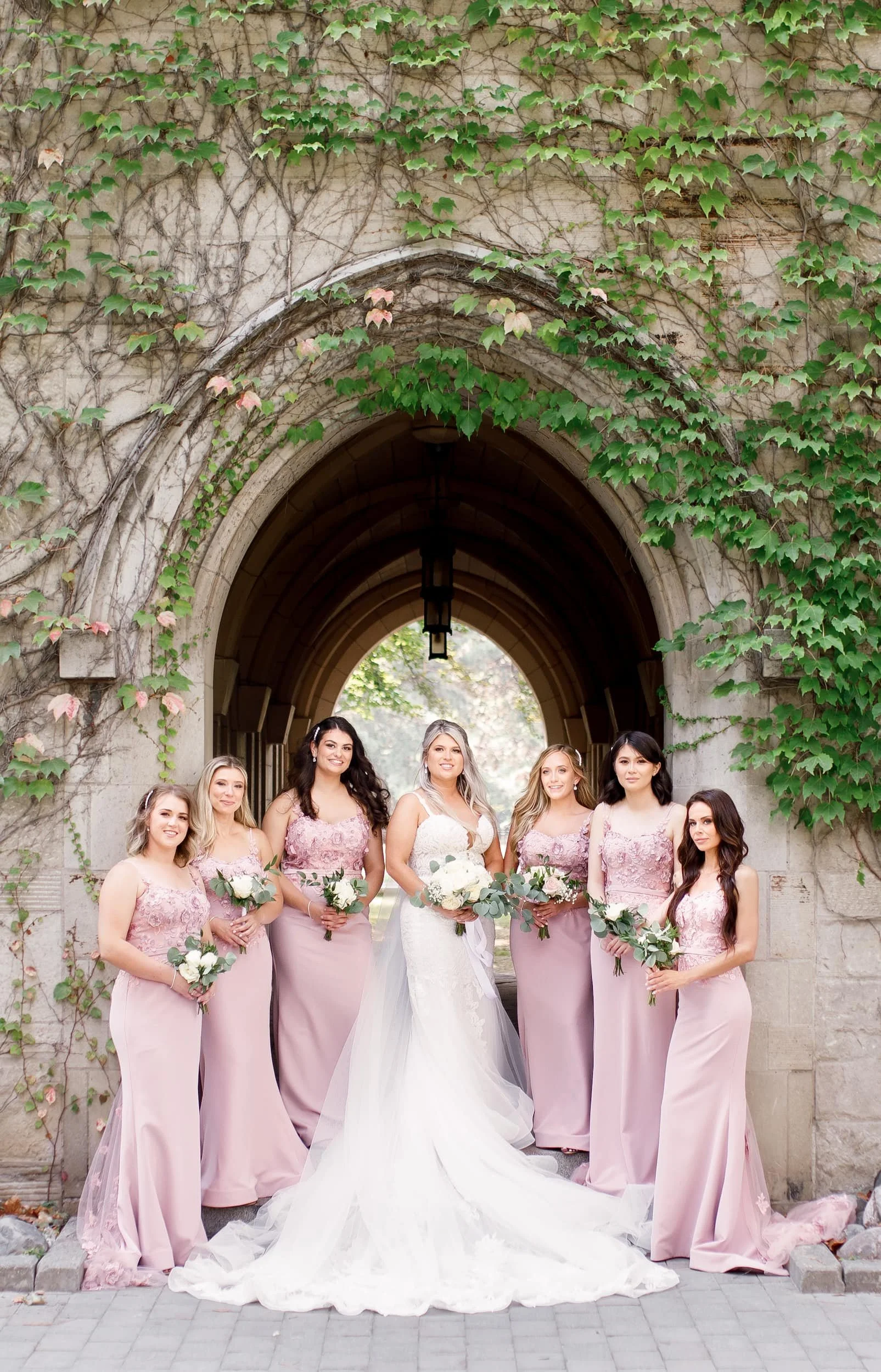Bride and bridesmaids standing beneath ivy-covered entrance at St. Michael’s College, University of Toronto in Toronto, Ontario
