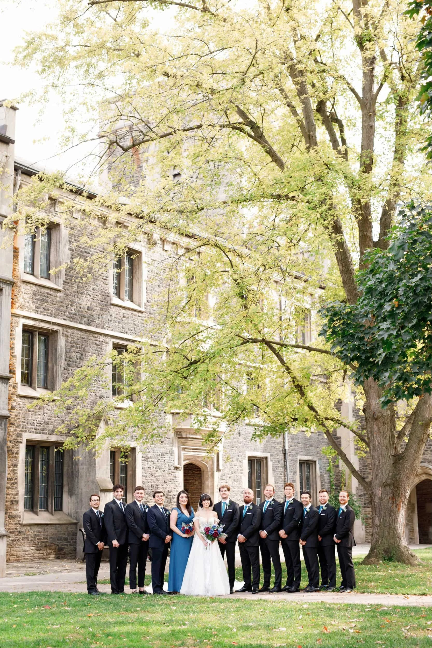 Wedding party gathered beneath mature trees at Victoria College, University of Toronto in Toronto, Ontario