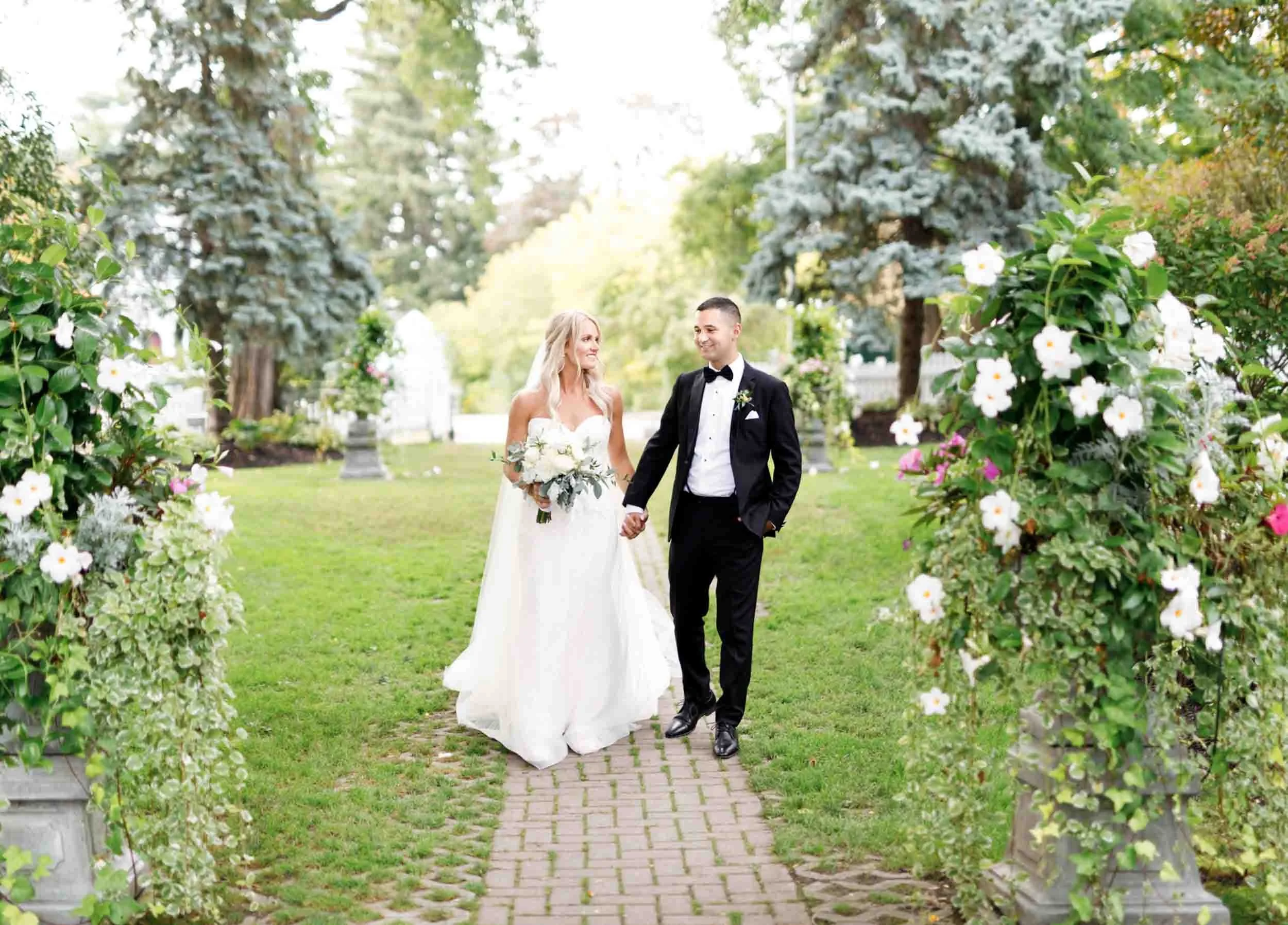 Bride and groom walking through garden pathway at The Doctor’s House in Kleinburg, Ontario