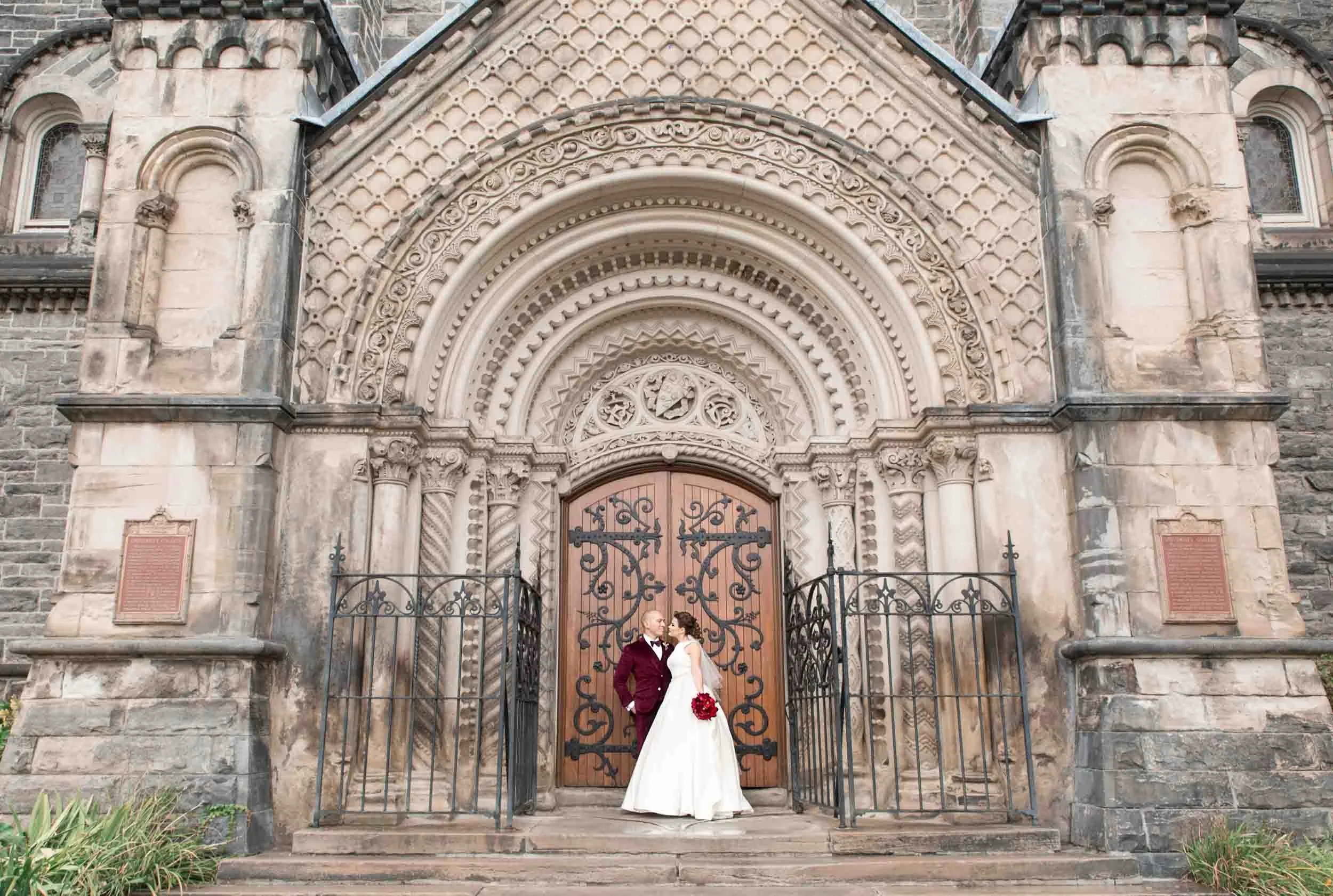 Bride and groom beneath ornate Gothic entrance at Knox College, University of Toronto in Toronto, Ontario