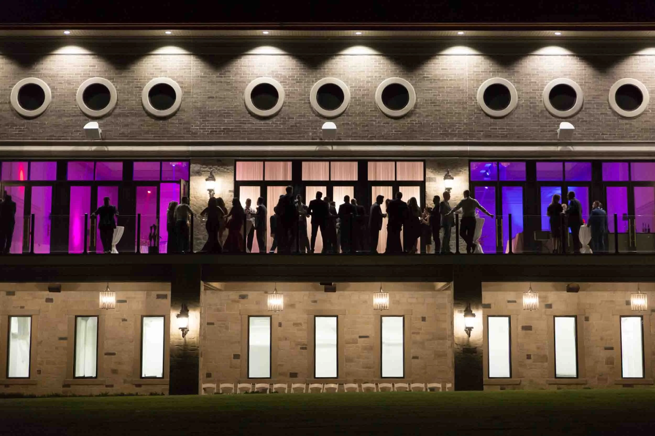 Nighttime exterior of the Arlington Estate reception with guests silhouetted on the balcony in Vaughan