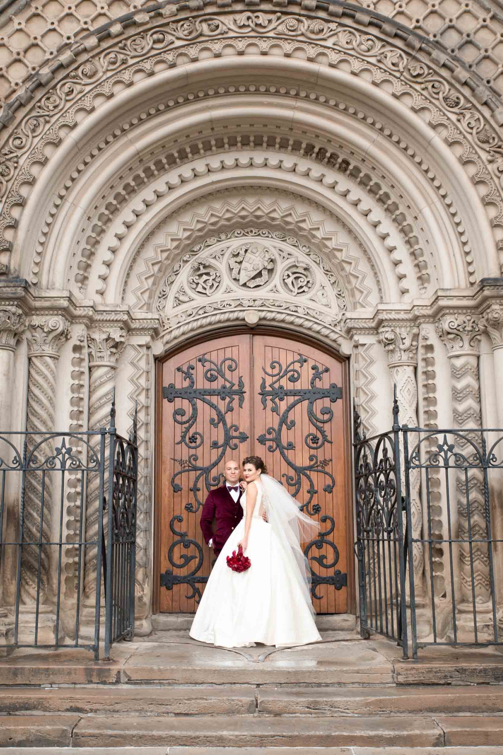 Wedding portrait in front of carved stone doorway at Knox College, University of Toronto in Toronto, Ontario