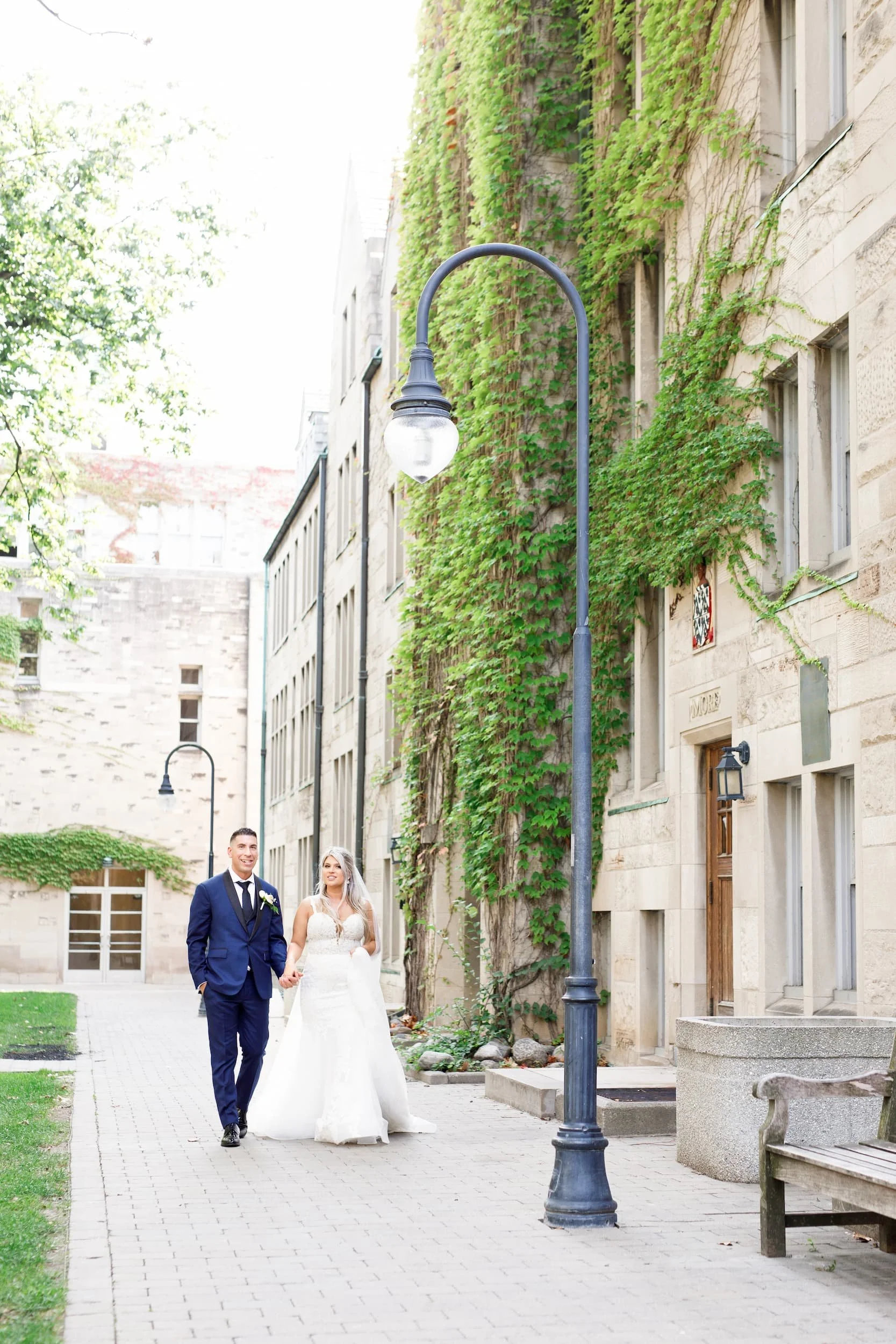 Bride and groom walking through ivy-lined courtyard at St. Michael’s College, University of Toronto in Toronto, Ontario