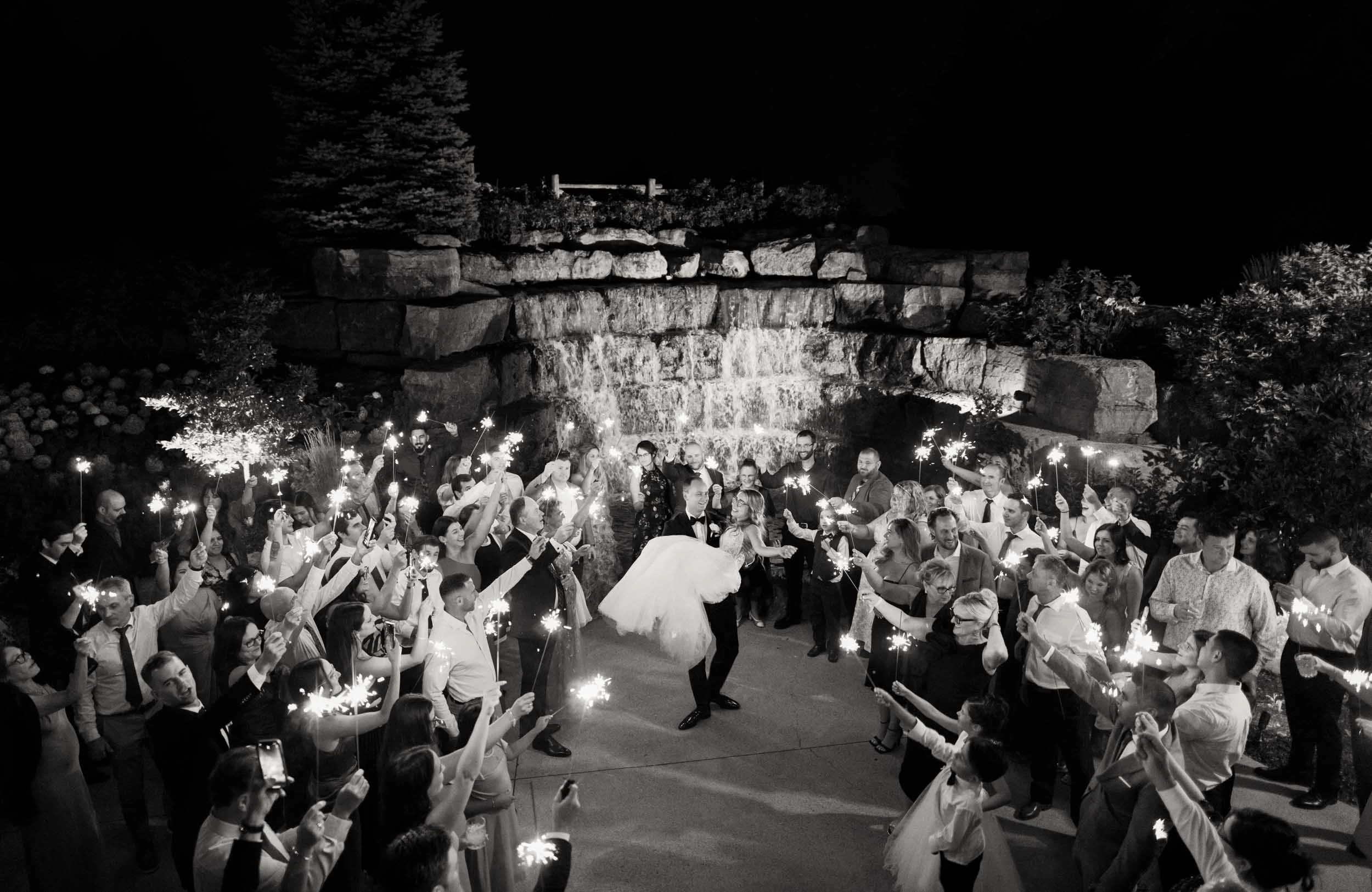 Black and white sparkler exit at night in front of waterfall at Whistle Bear Golf Club wedding in Cambridge, Ontario