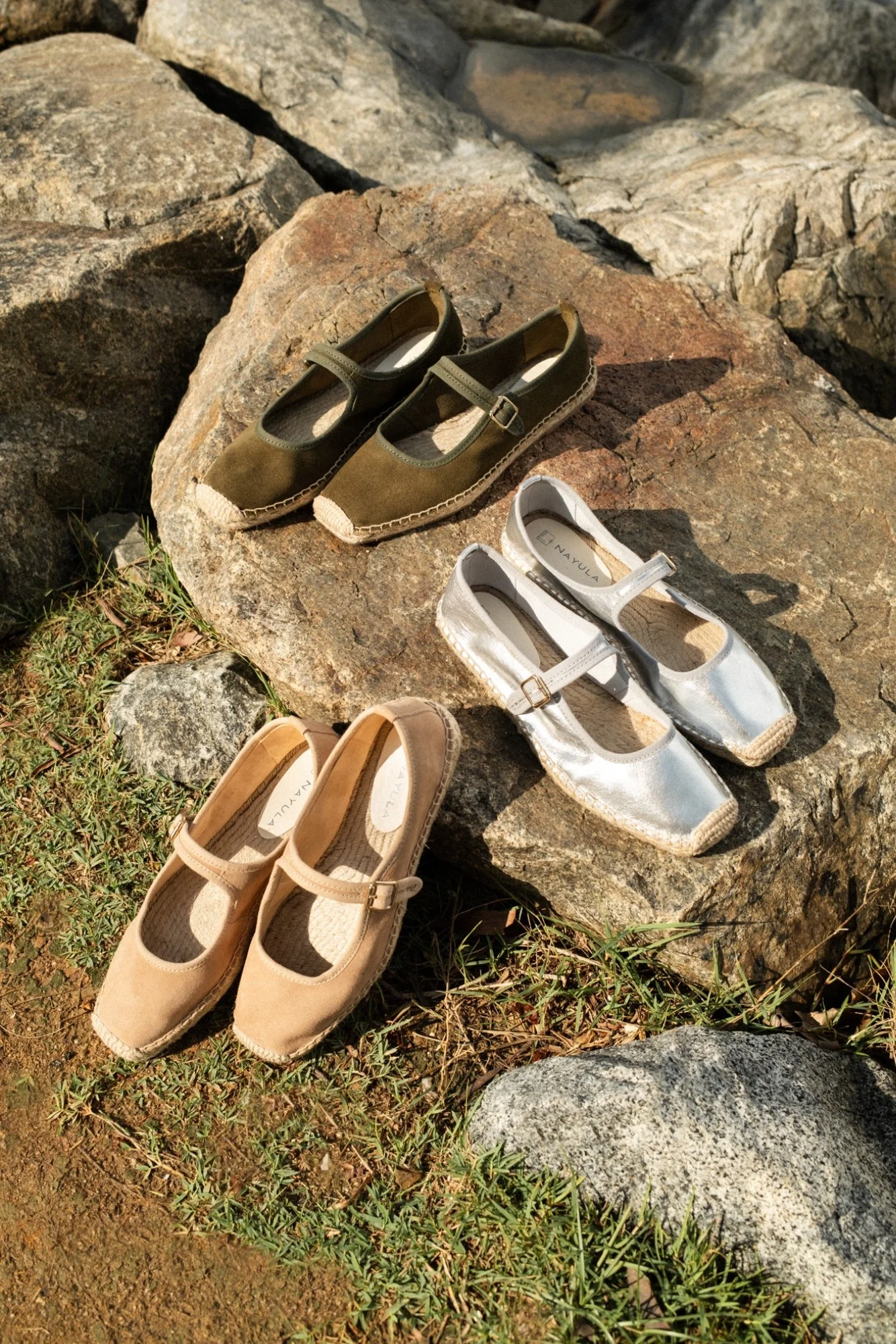 A collection of women's shoes placed on rocks outdoors, including beige, white, and olive green Mary Jane shoes.