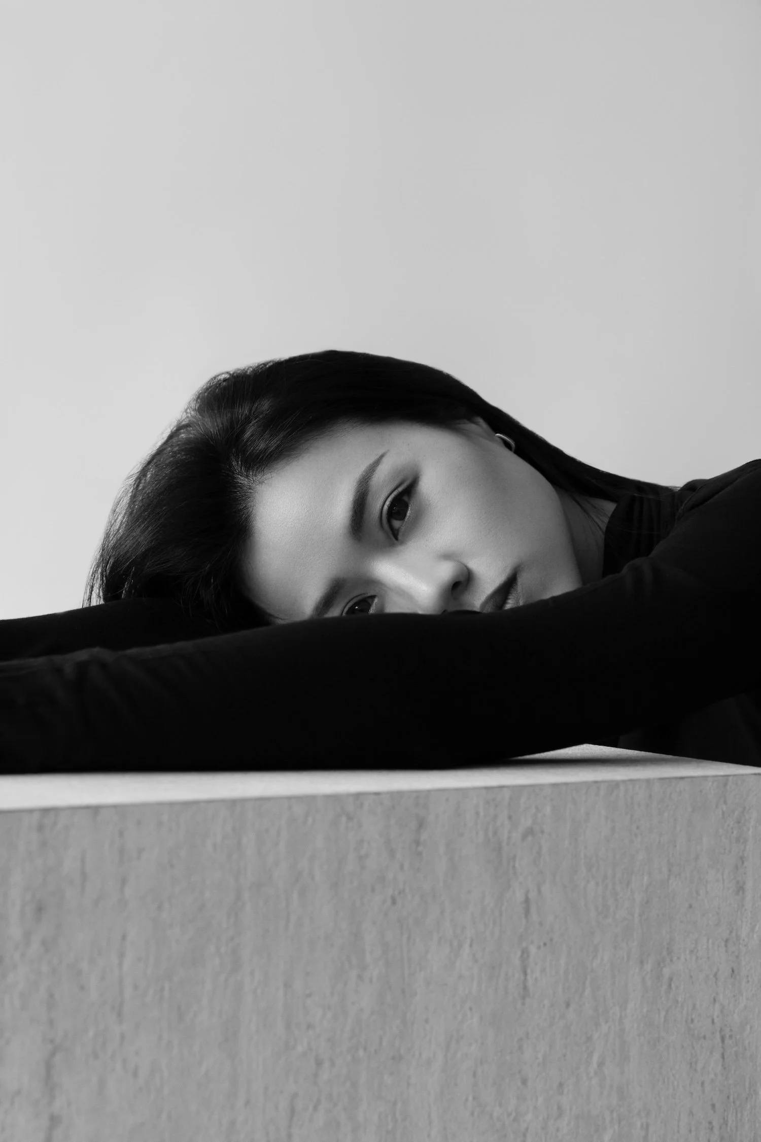 Black and white portrait of a woman with long dark hair, lying on a surface with her arm extended over the edge.