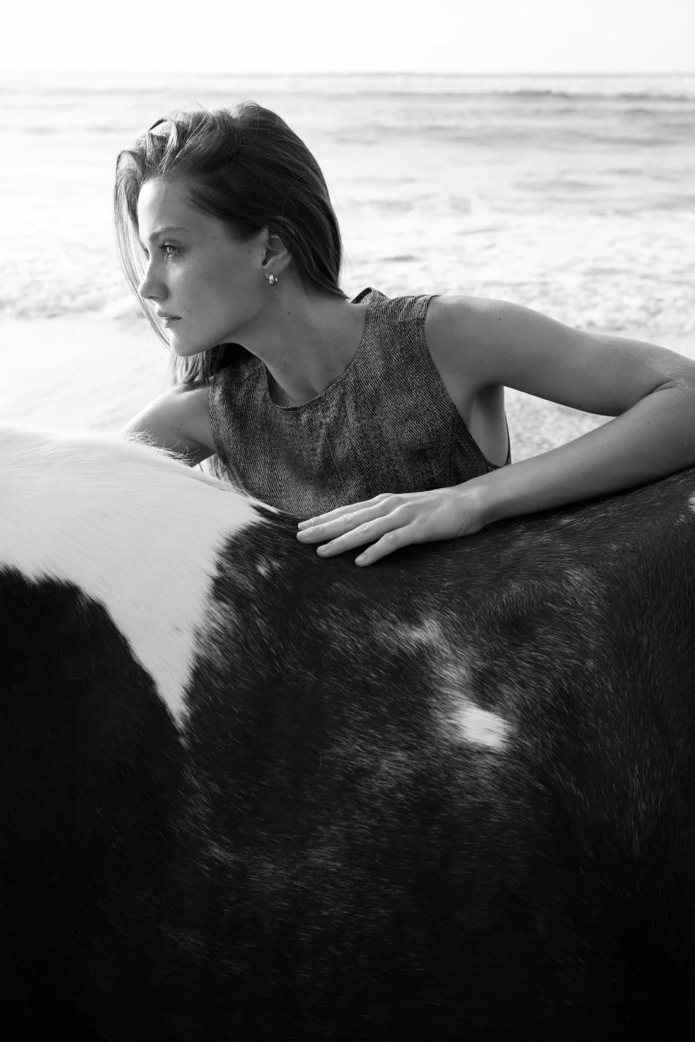 A woman lying on a cow at the beach, black and white photograph.