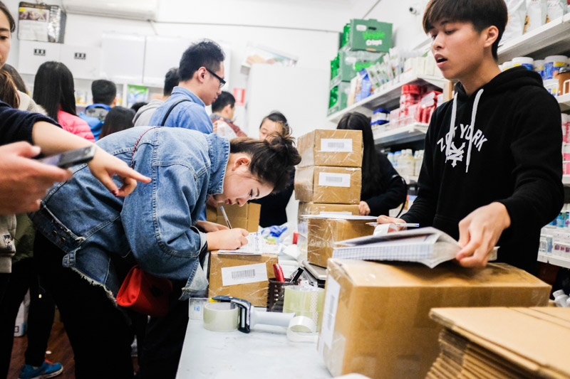 A customer surrounded by packed boxes to be mailed to China fills in a courier docket at the ‘Chang Jiang International Express’ store in Melbourne. Asanka Brendon Ratnayake for The New York Times.