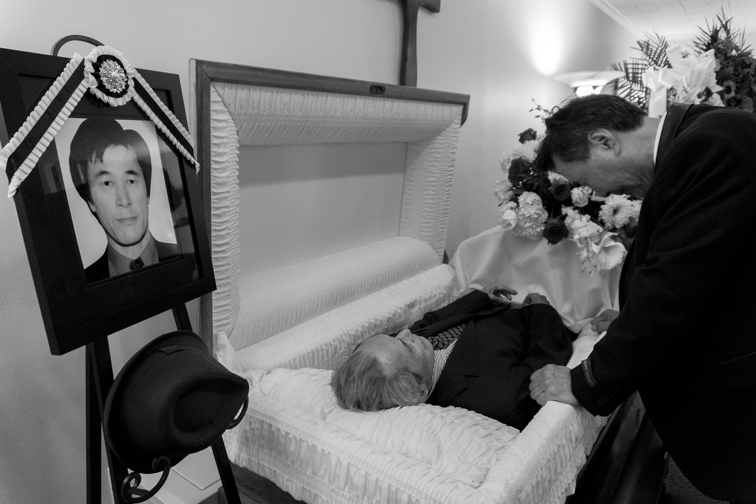  Suksoo Kim, who Chinsoo Kim had the closest relationship with out of his surviving siblings, looks at his older brother’s face for the final time before the casket is closed. A picture of Chinsoo Kim looks over the scene. Chinsoo Kim died on 9/14/17