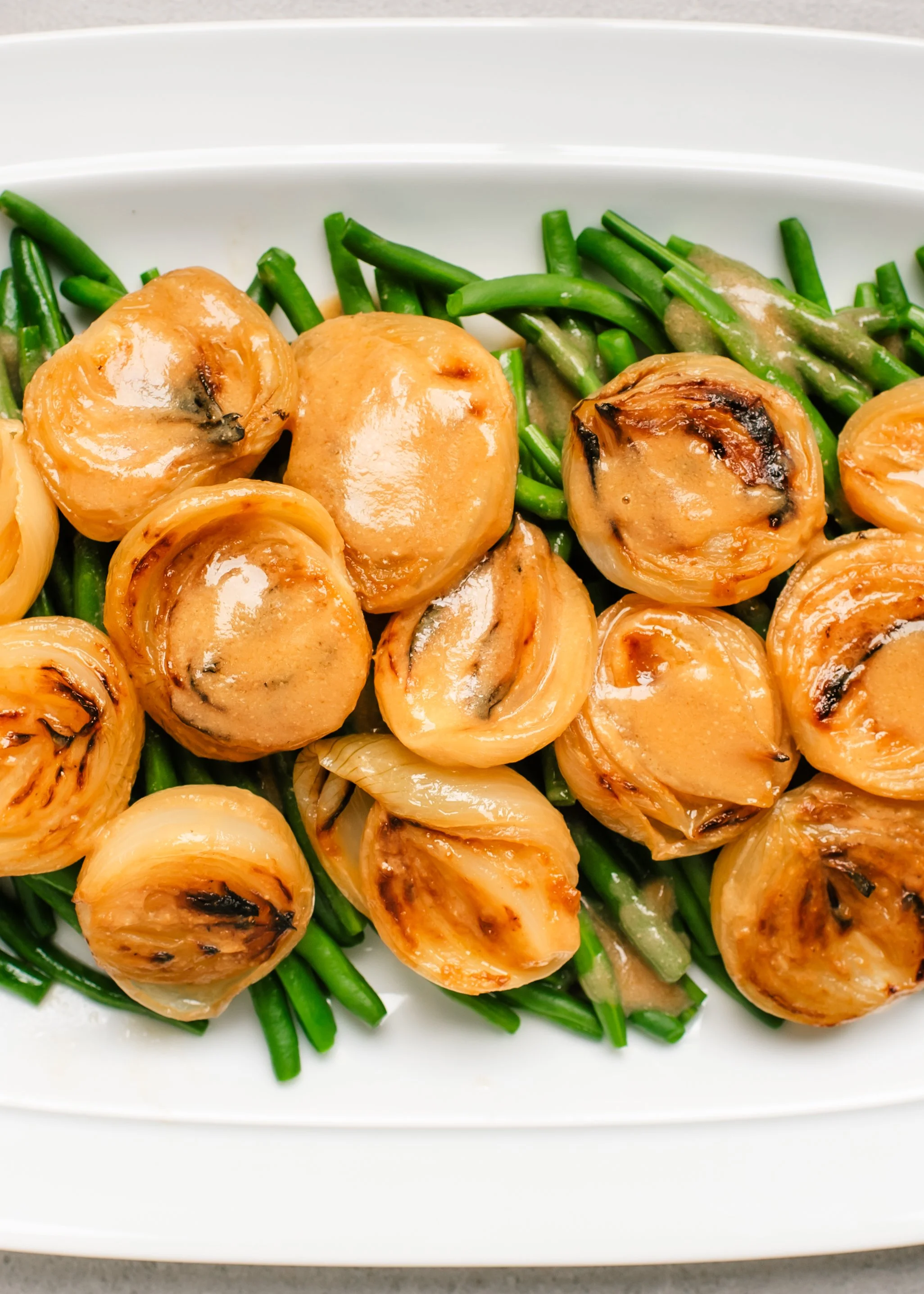 Roasted white onion halves with sauce on green beans on white platter