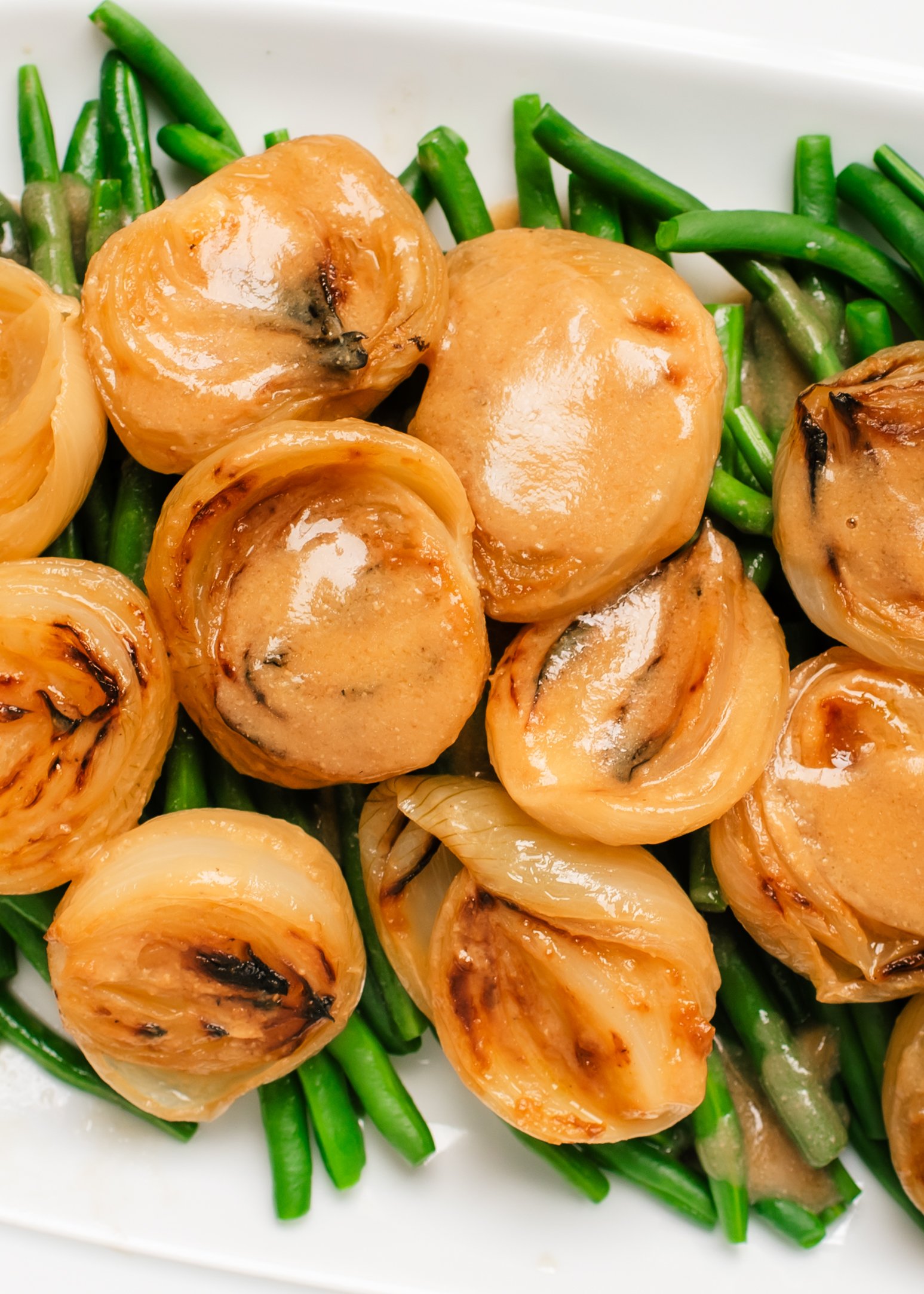 Roasted white onion halves covered in sauce on top of blanched green beans on white platter