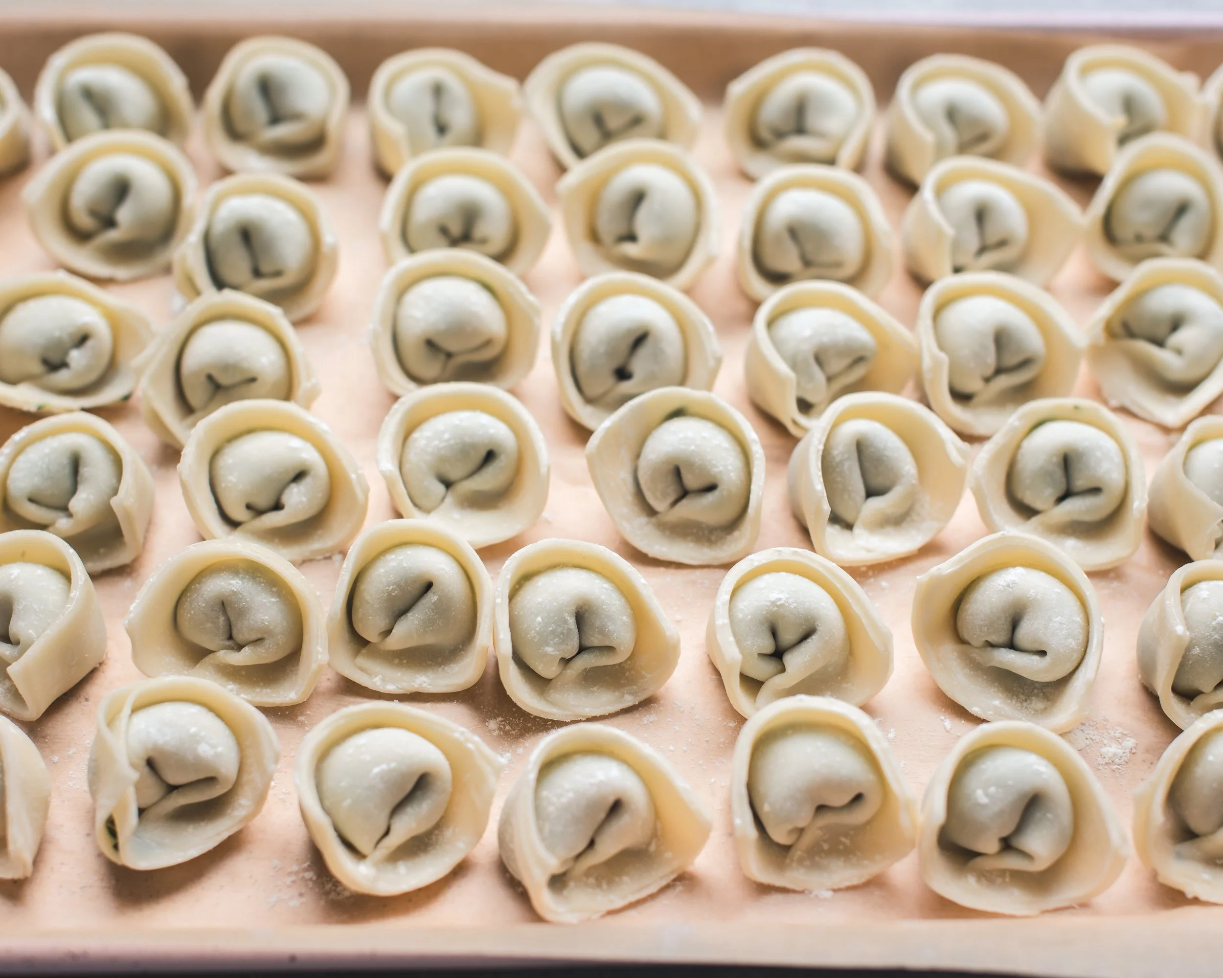 Uncooked wontons on a light pink parchment lined sheet pan.