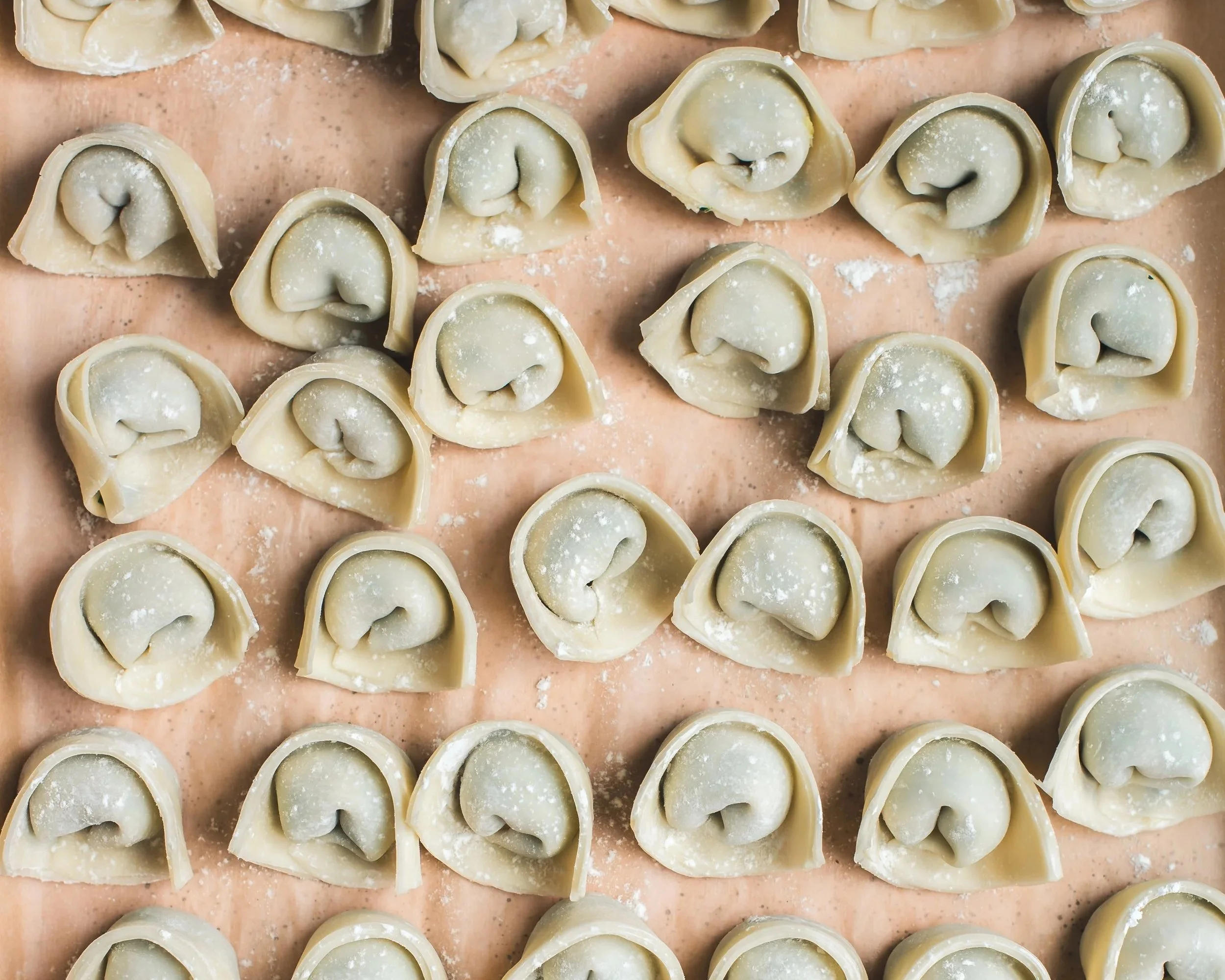 Uncooked wontons on light pink parchment lined sheet pan