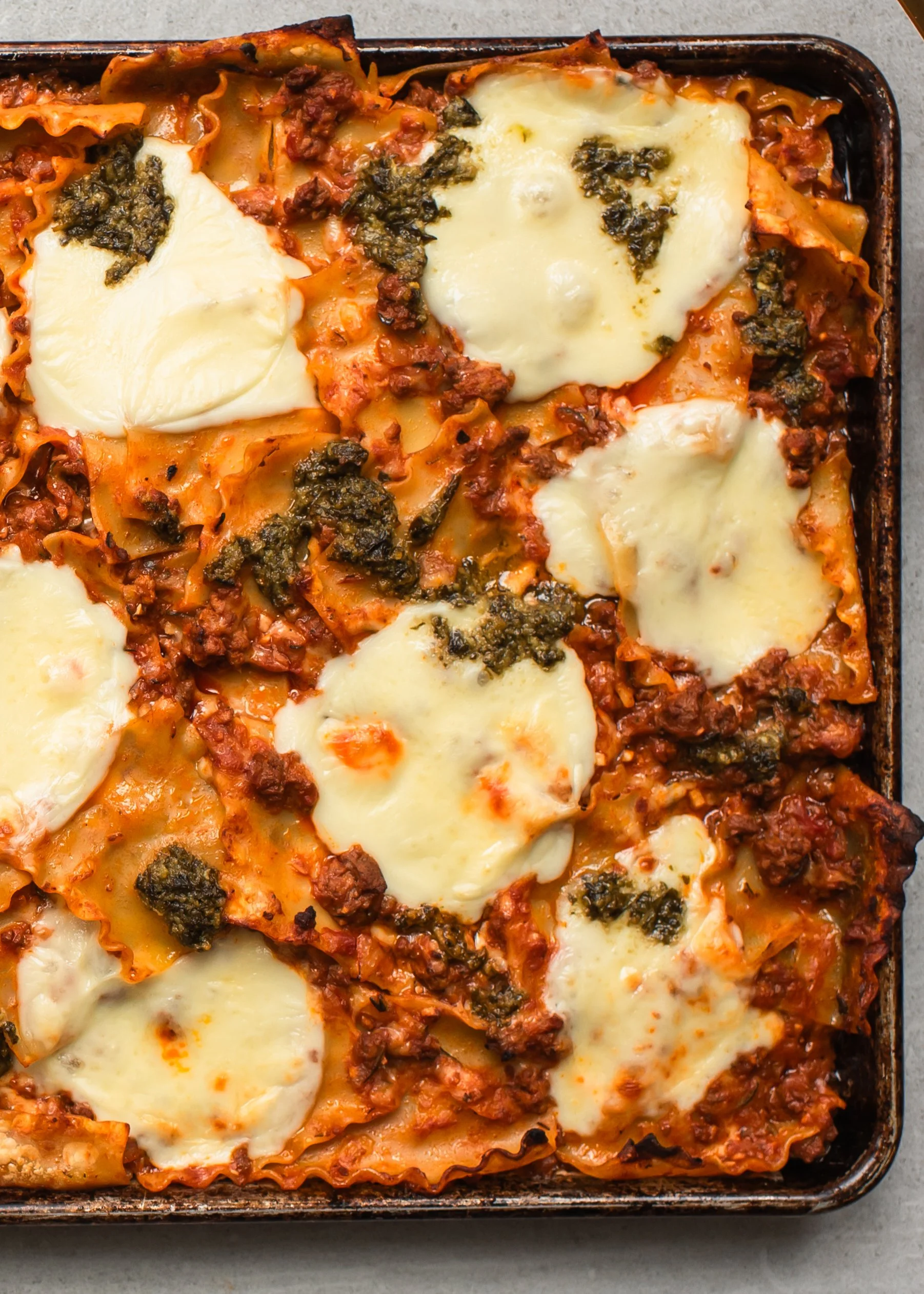 Baked pasta casserole with melted cheese, meat sauce, and pesto on top in a baking dish.