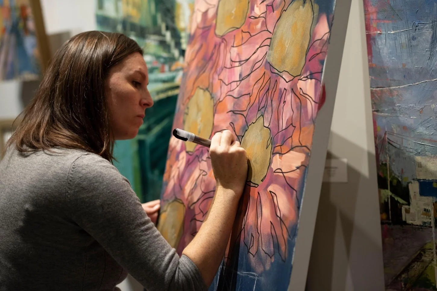 Artist Meg Davies painting a flower on a canvas in an art gallery.